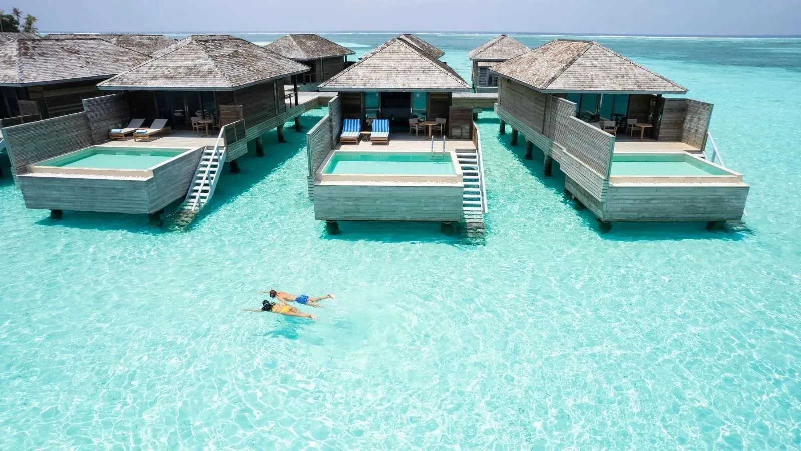 The overwater pool villas from above, with a swimmer in the turquoise lagoon