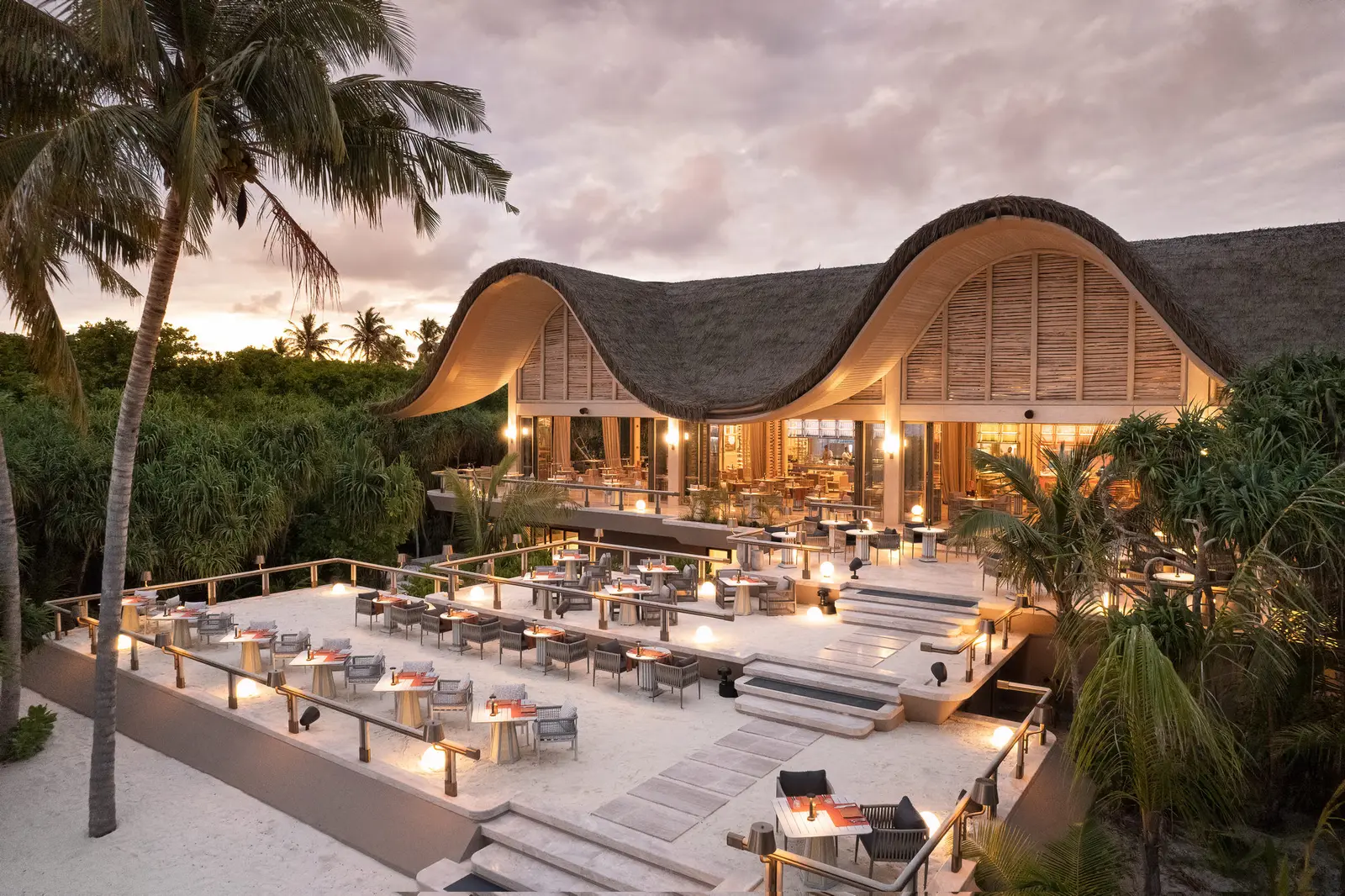 FLOW outdoors in the evening, its wavy roof and lit tables
