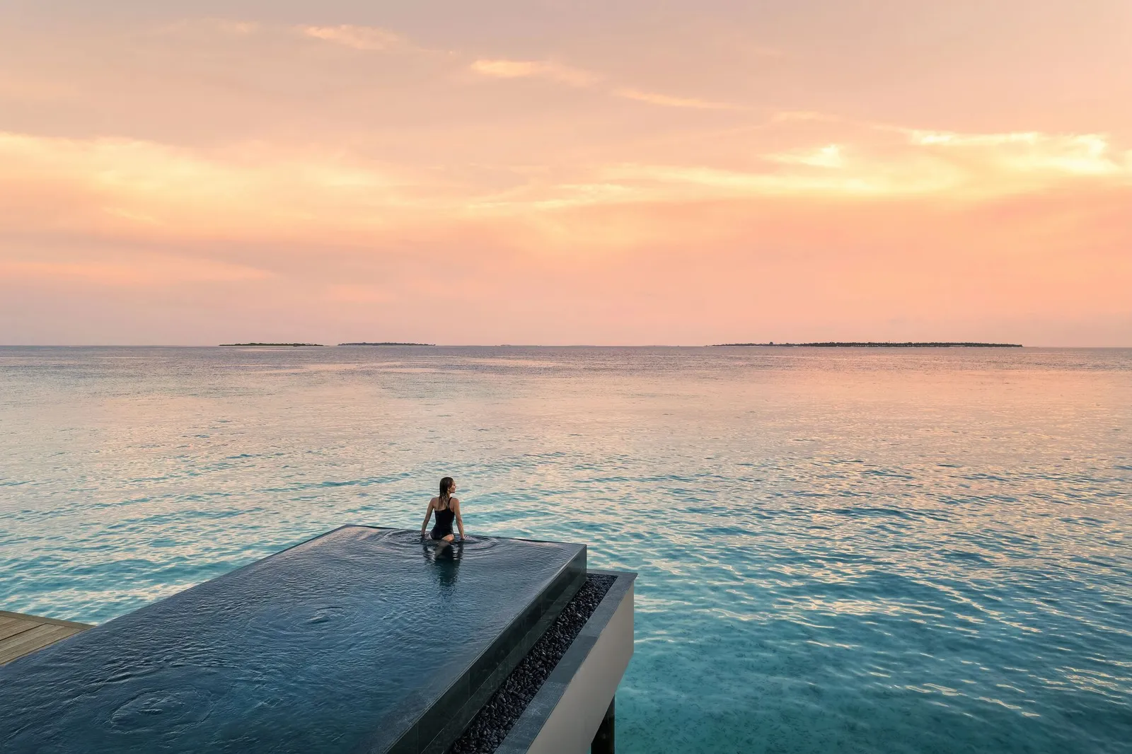 A guest in a water villa’s infinity pool at sunset