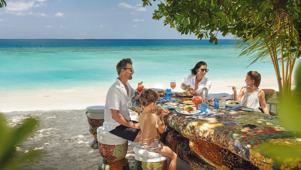 A family at lunch on the beach, turquoise sea behind