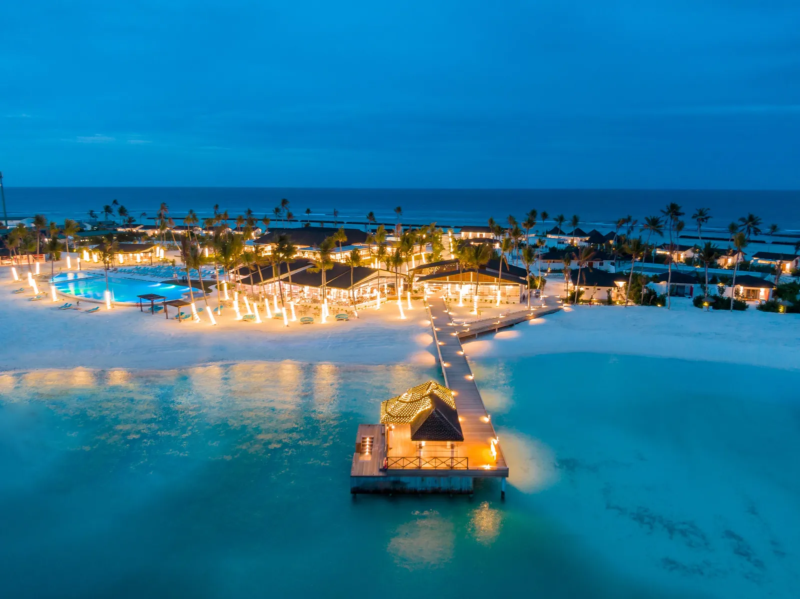 The island from above at dusk, the pool and pavilions lit and the jetty out to a pavilion on the lagoon