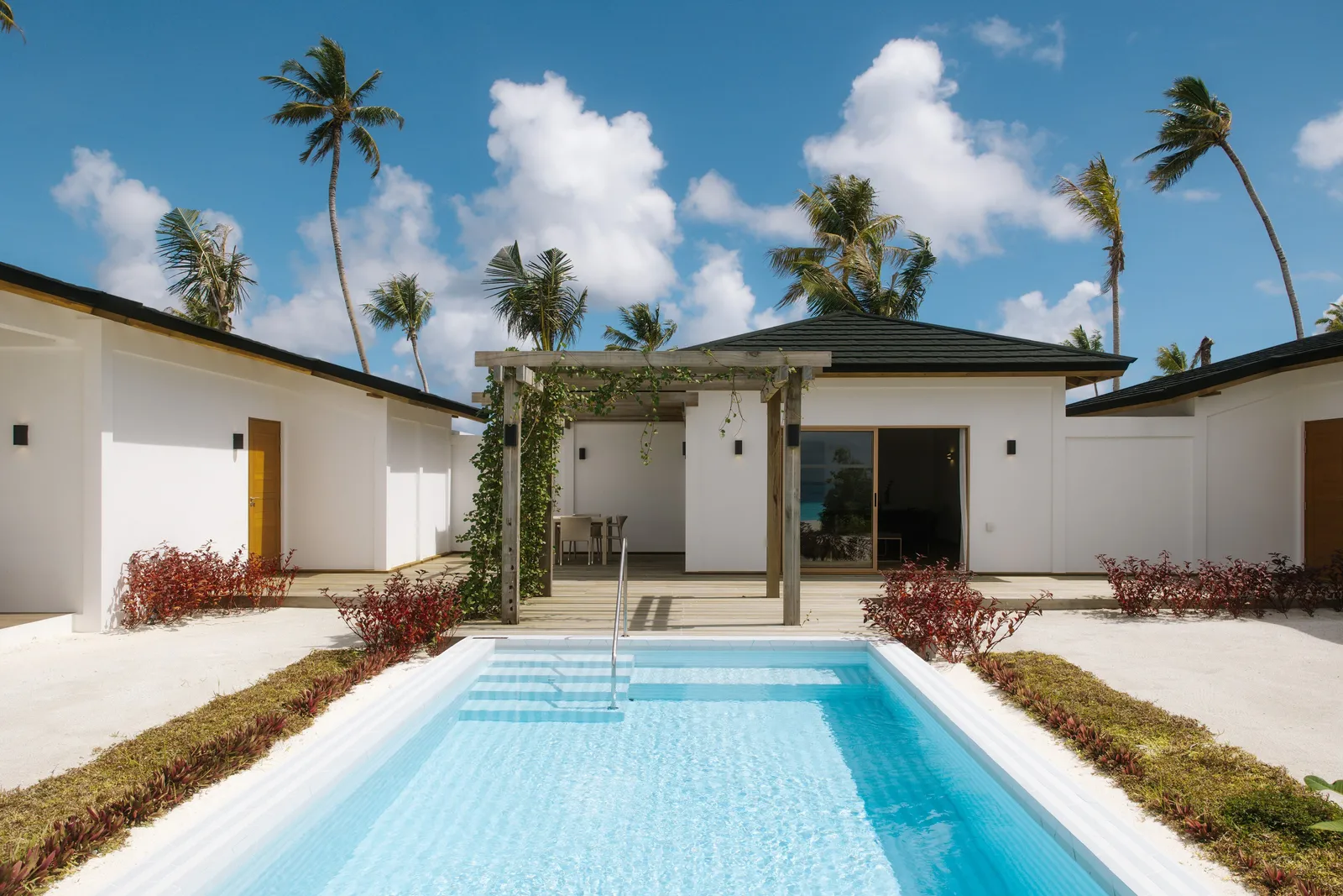 The Beach Residence’s pool in its courtyard, the white villa and the palms behind