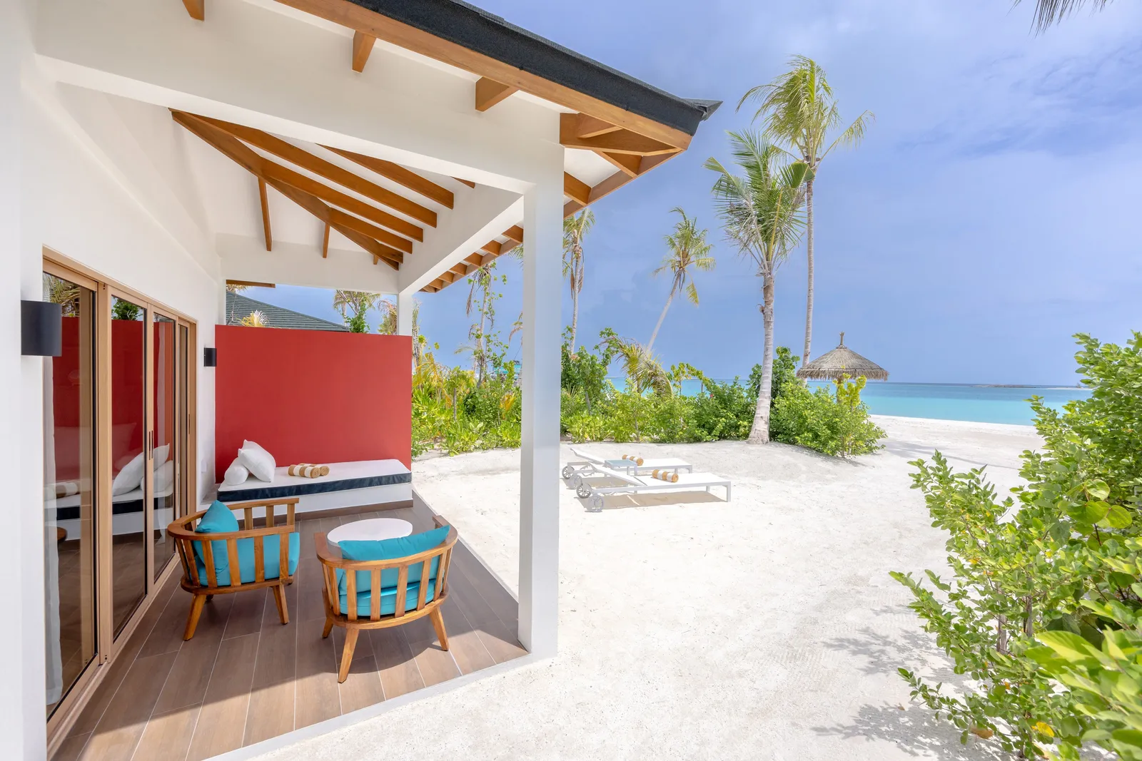 A Beach Suite’s veranda with its red wall, 2 armchairs and the beach through the palms