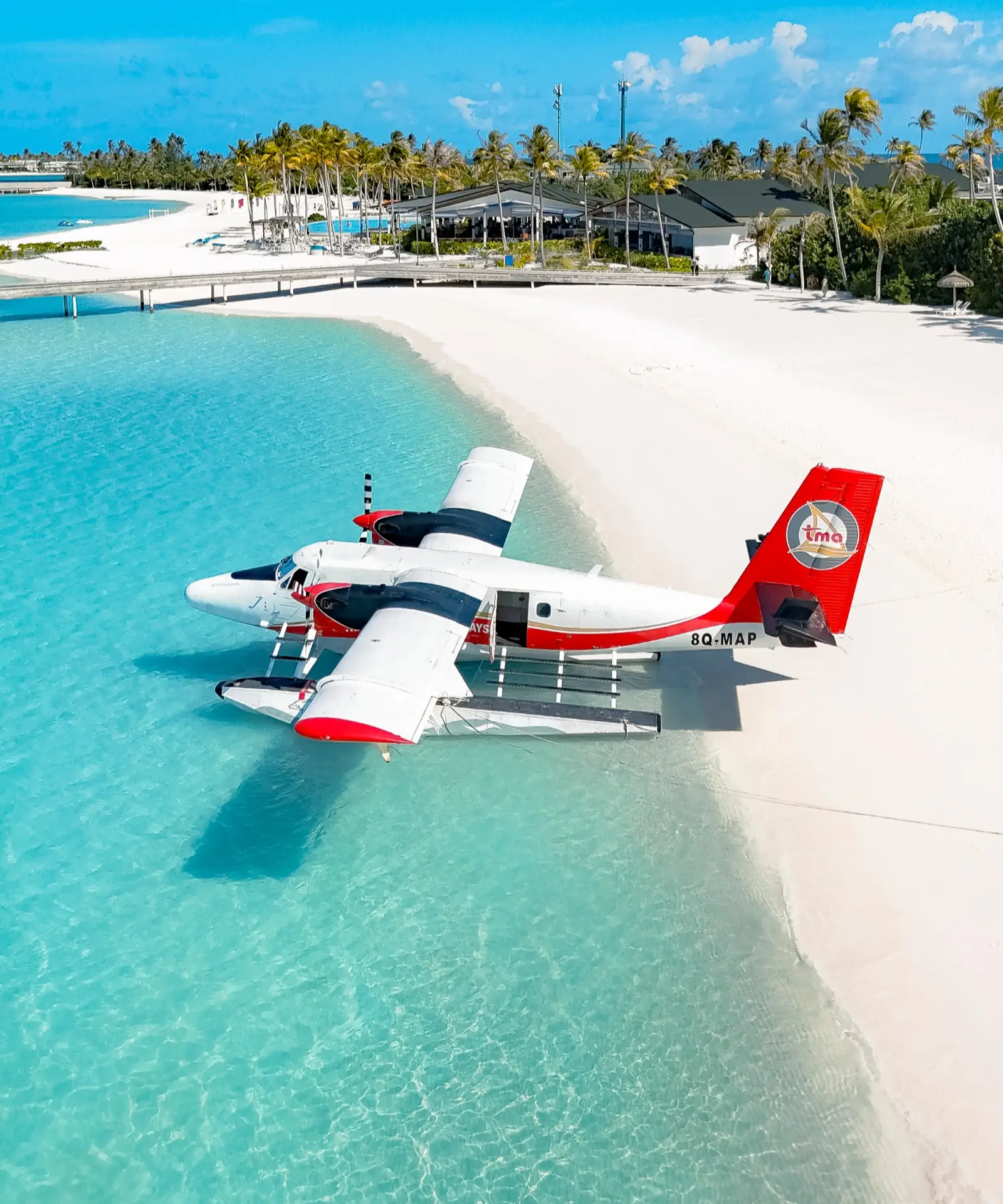 A red and white seaplane moored in the shallows off the beach