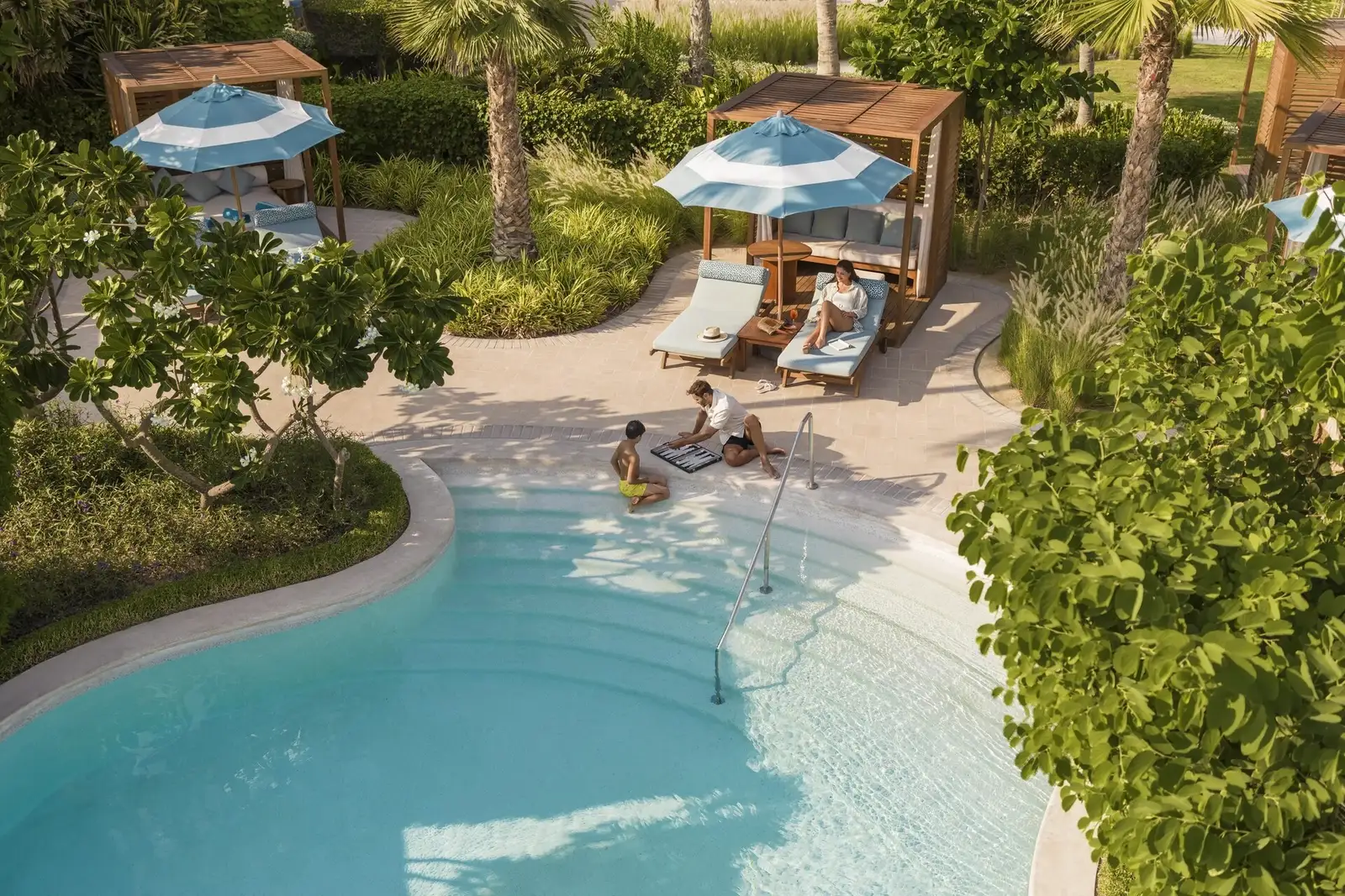 A pool among palms with cabanas, seen from above