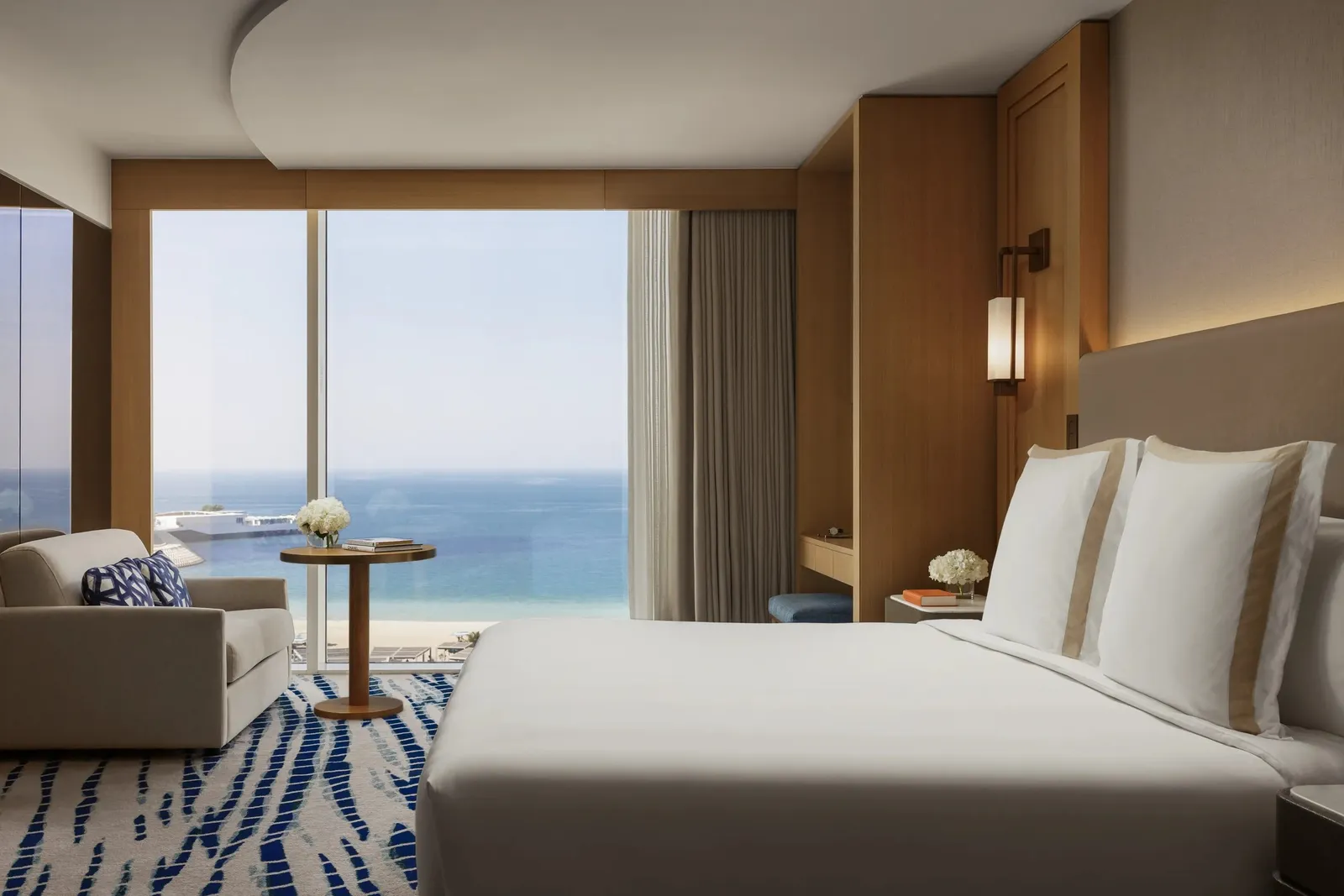 An Ocean Deluxe room with its white bed before the glass onto the sea