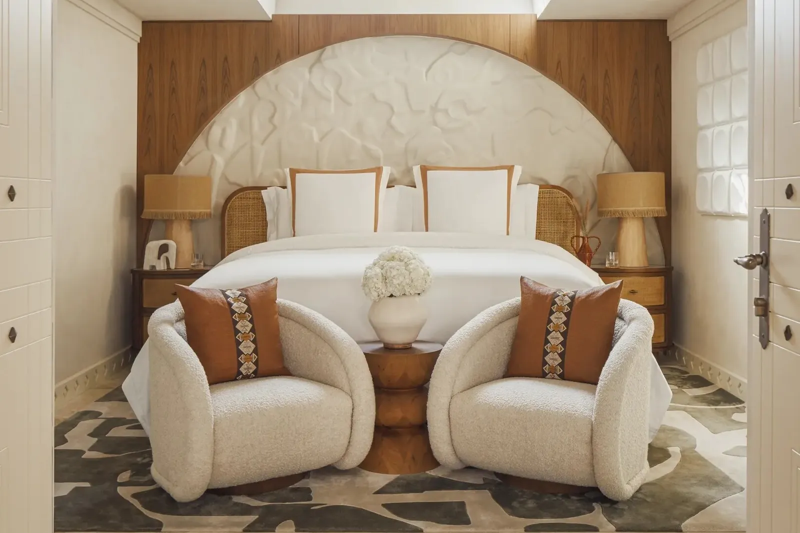 An Al Bahar villa bedroom with the bed under a plaster arch and 2 armchairs