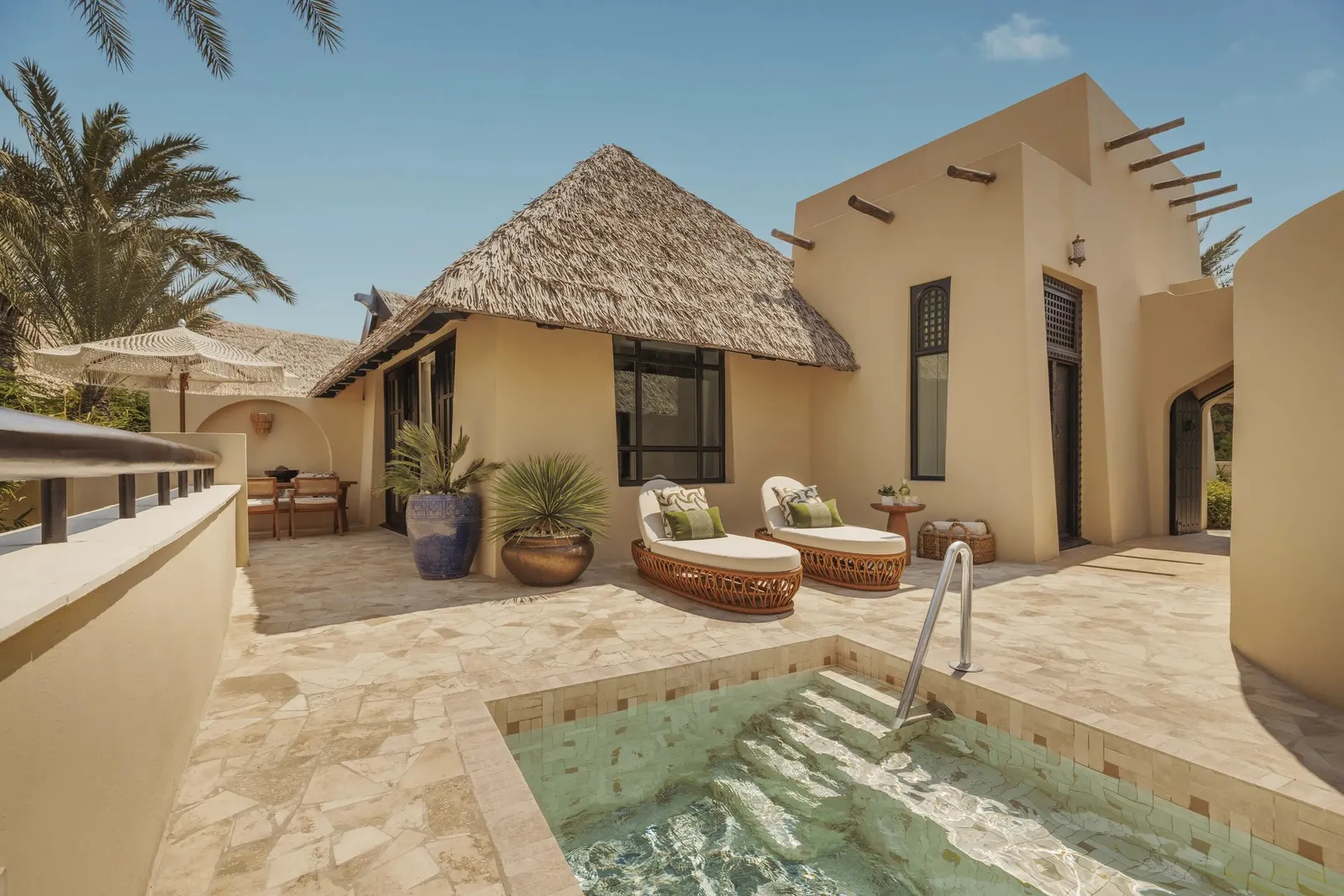 A villa terrace with its pool, loungers and a thatched roof
