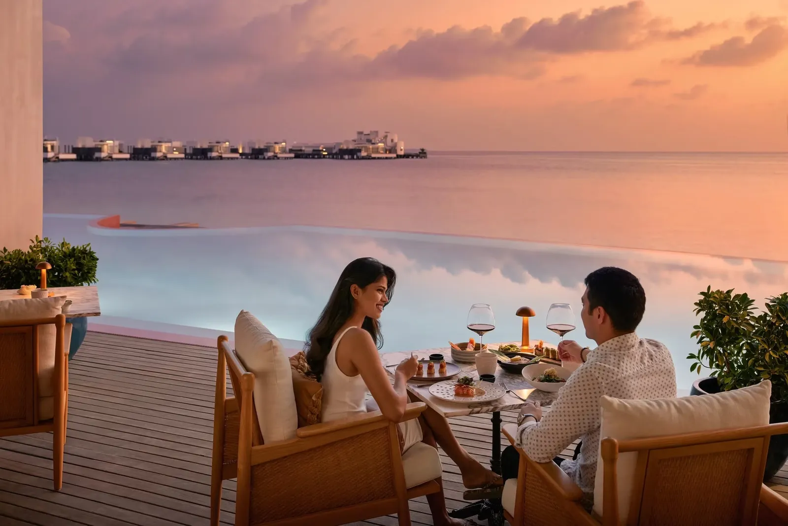 A couple at dinner on Kayto’s terrace at sunset, the water villas on the horizon