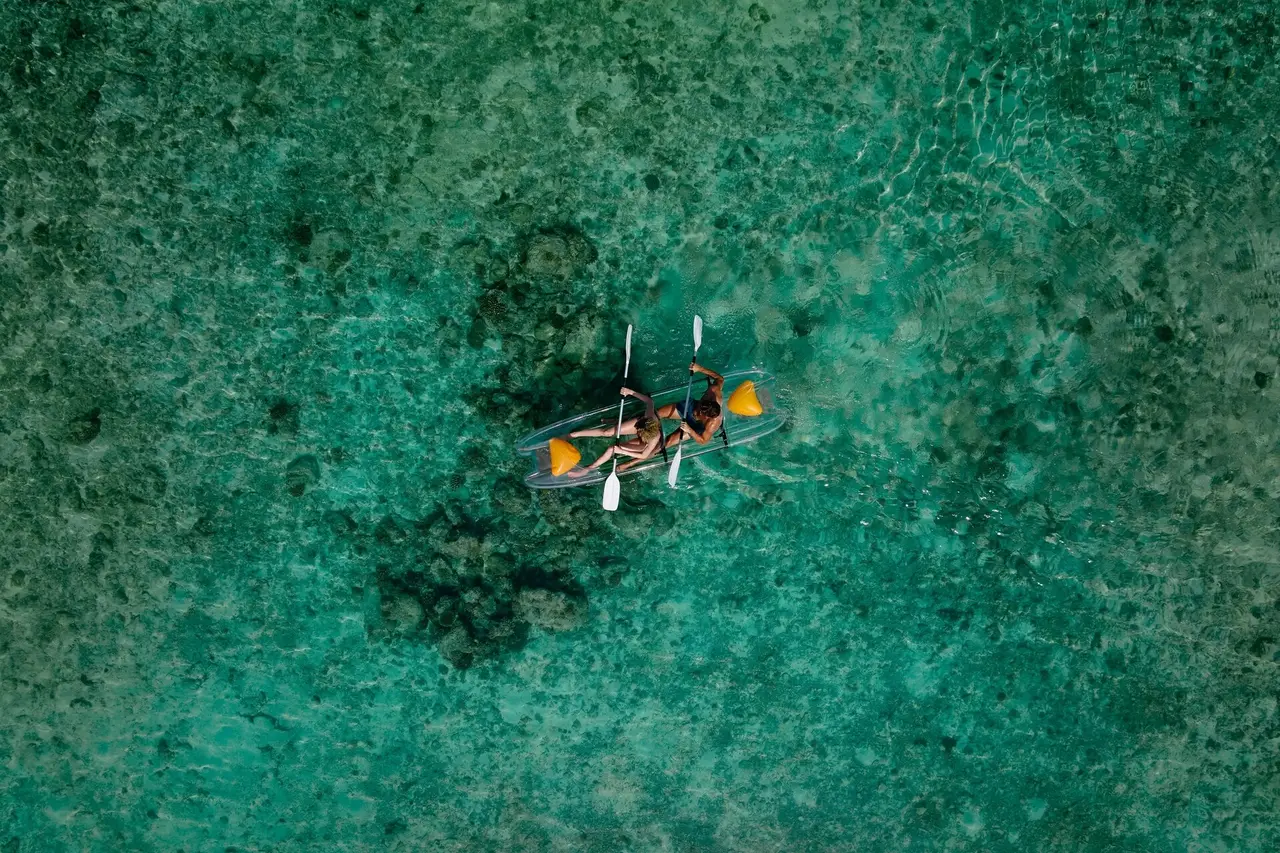 2 people in a clear kayak above the dark patches of the reef