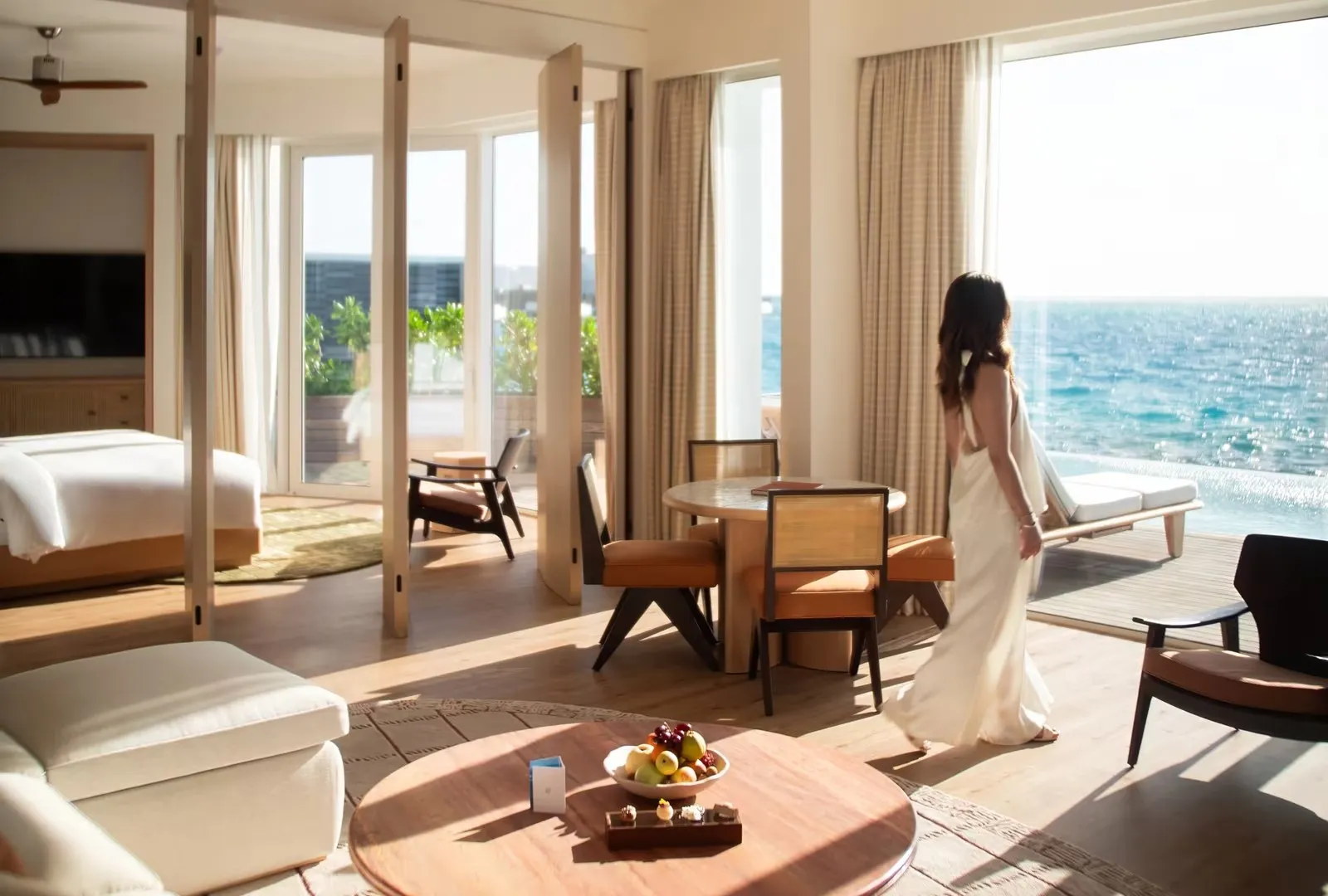 A woman in a white dress stepping onto the villa terrace from a living room open to the ocean