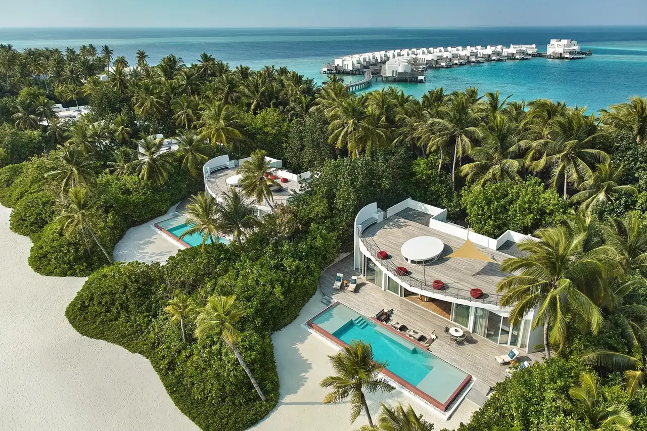 2 beach residences from above, their pools among the palms and the water villas behind