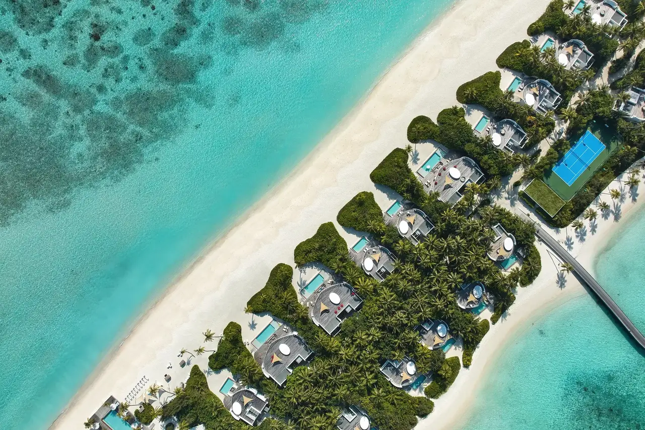 The row of beach villas from above, each pool set in greenery above the white sand