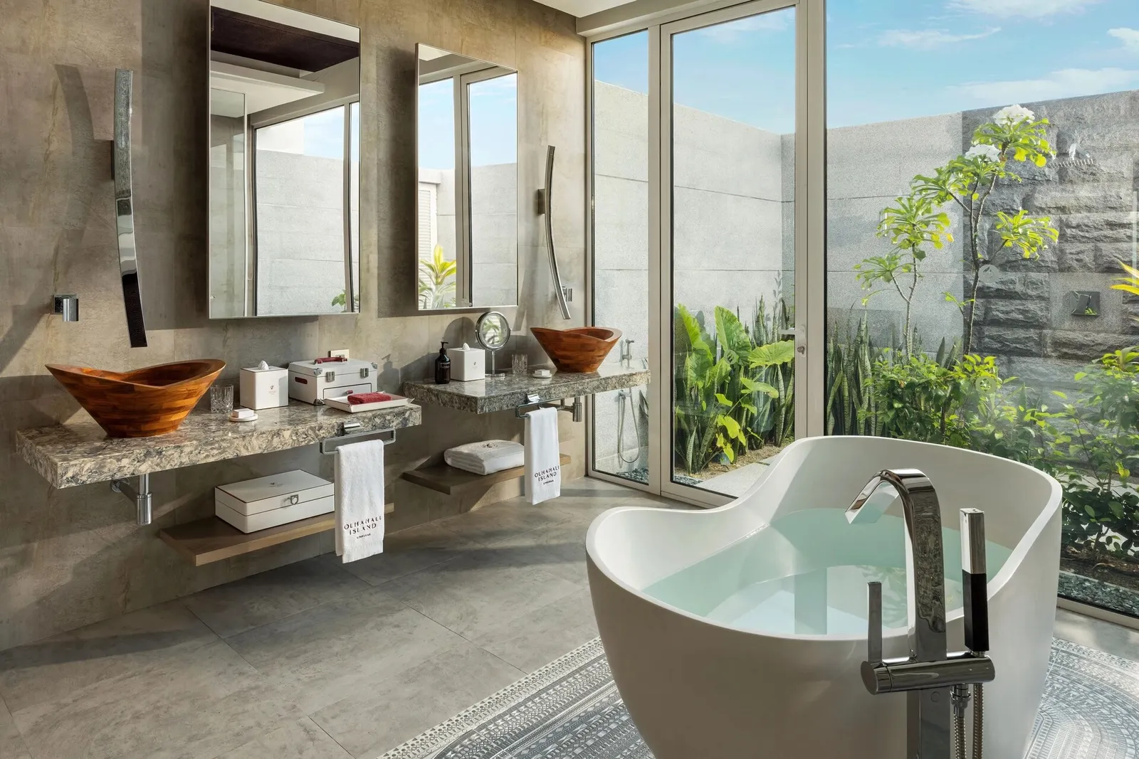 The Water Residence bathroom, its white tub, basins on a stone counter and plants beyond the glass