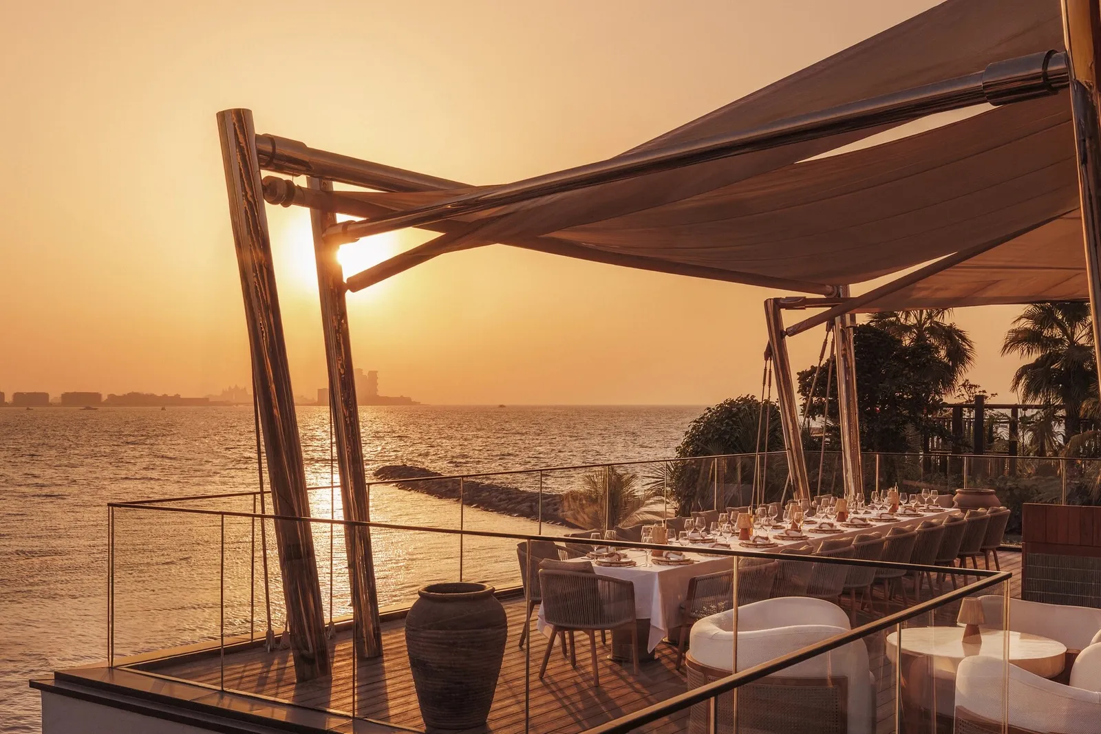 A terrace laid for dinner under a sail at sunset