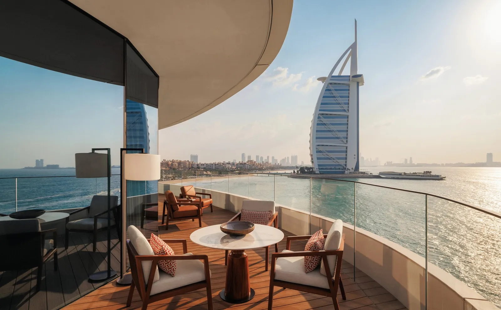 A curved terrace with a table and armchairs, the Burj Al Arab on the sea