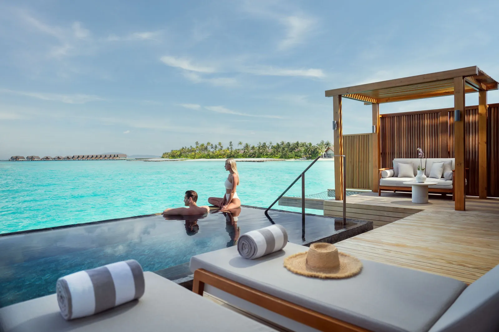 A couple in an overwater villa’s infinity pool, the sea beyond the edge