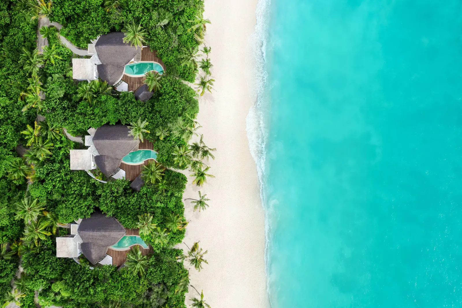 3 beach villas from above, each with its pool in the greenery, beside the white sand