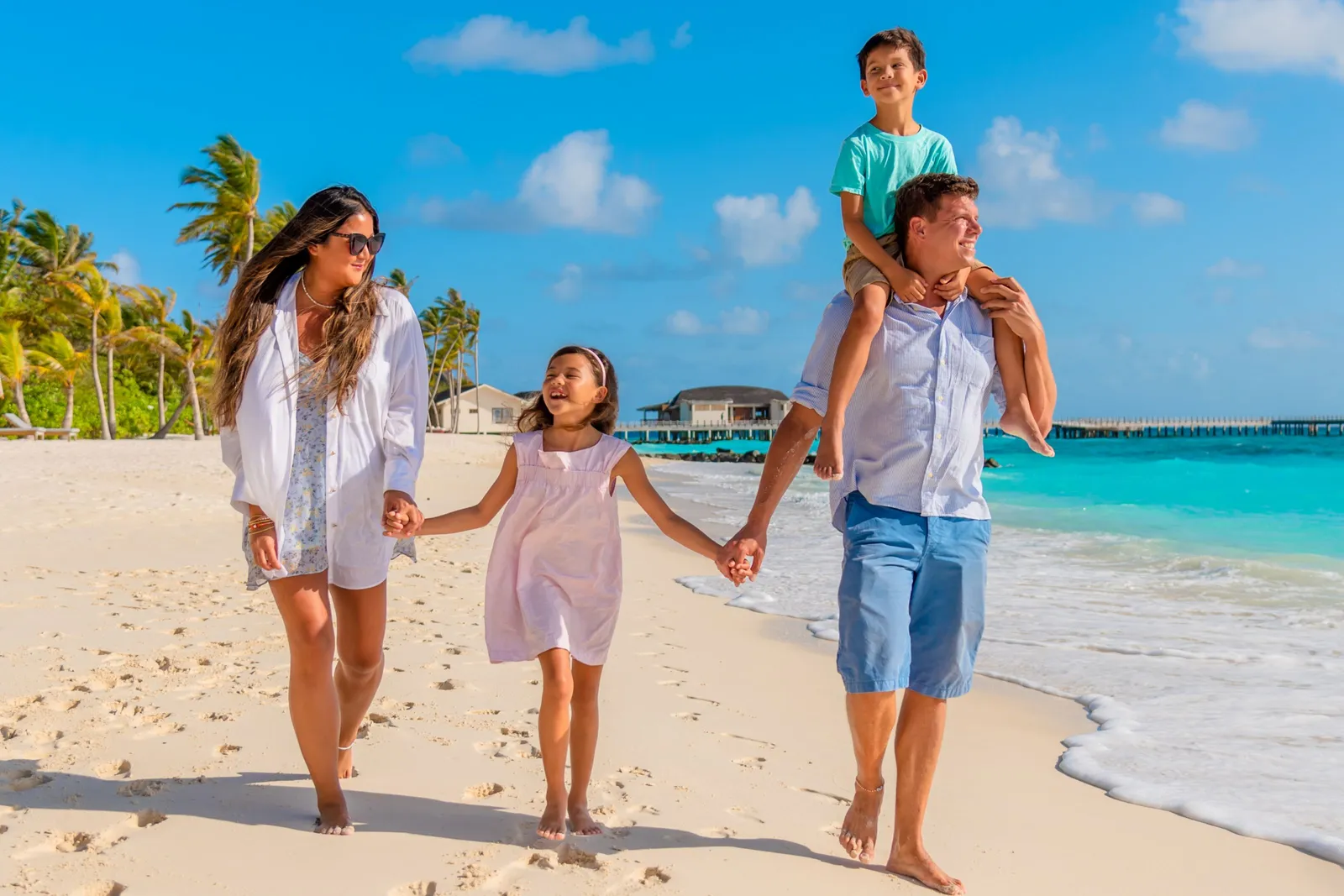 A family walking along the shoreline, the boy on his father’s shoulders