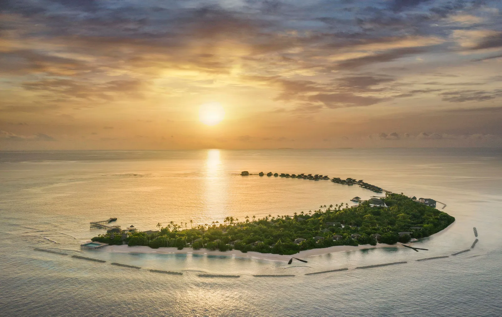 Vagaru from the air at sunset: the long green island on its lagoon, the sun low over the sea