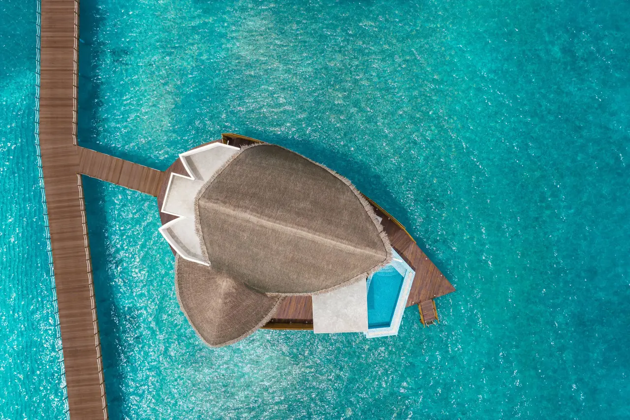 An overwater villa from above, its roof and deck pool in the middle of the lagoon