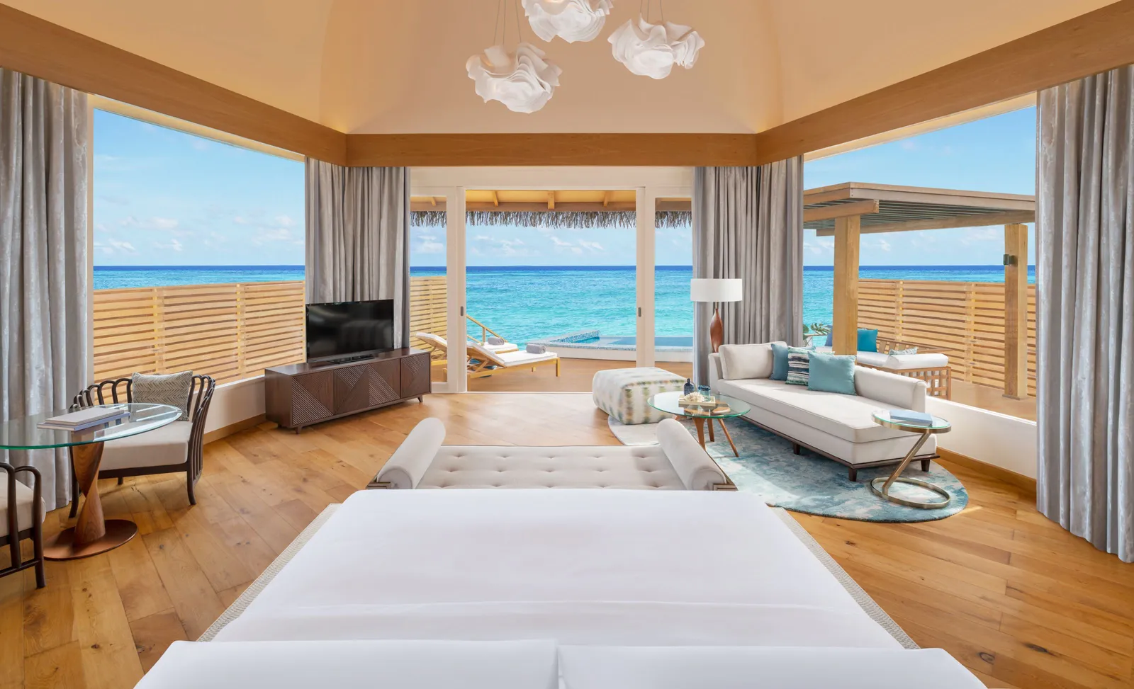 An overwater villa’s bedroom, the bed facing the windows onto the deck and the sea