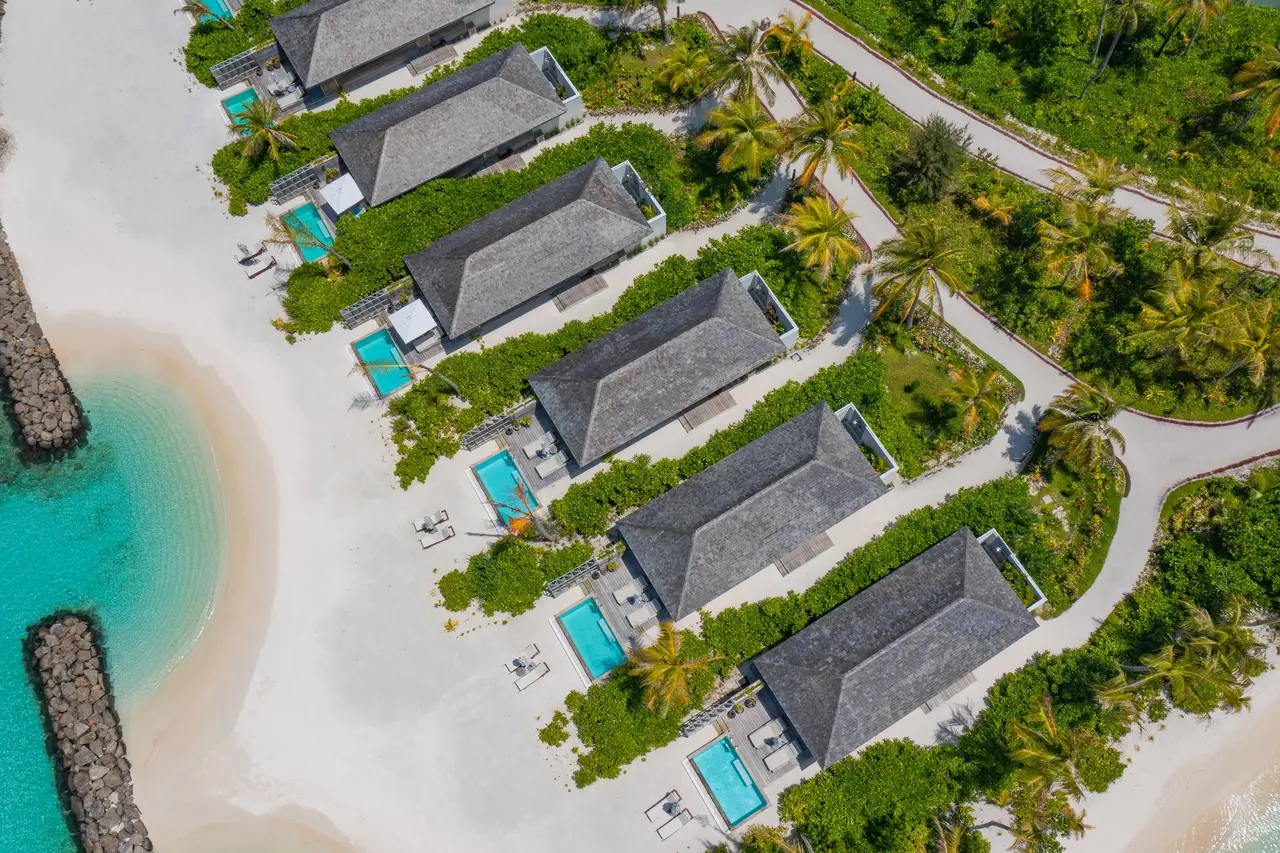 The Beach Pool Villas from above, grey roofs between the greenery and the white sand