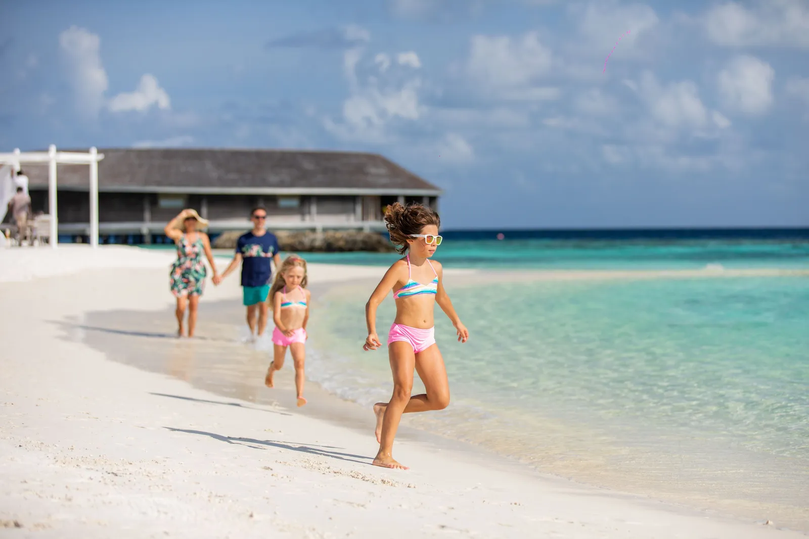 A family running along the shoreline, the restaurant over the sea behind