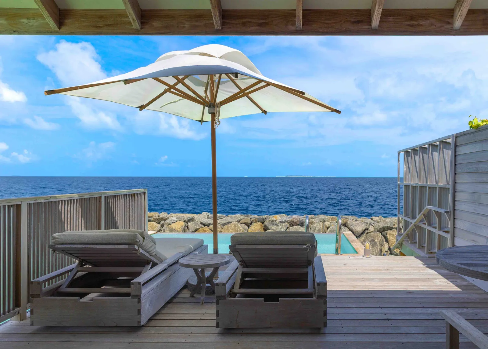 An Ocean Pool Villa’s deck, the parasol and loungers; beyond the railing, the breakwater rocks and the sea