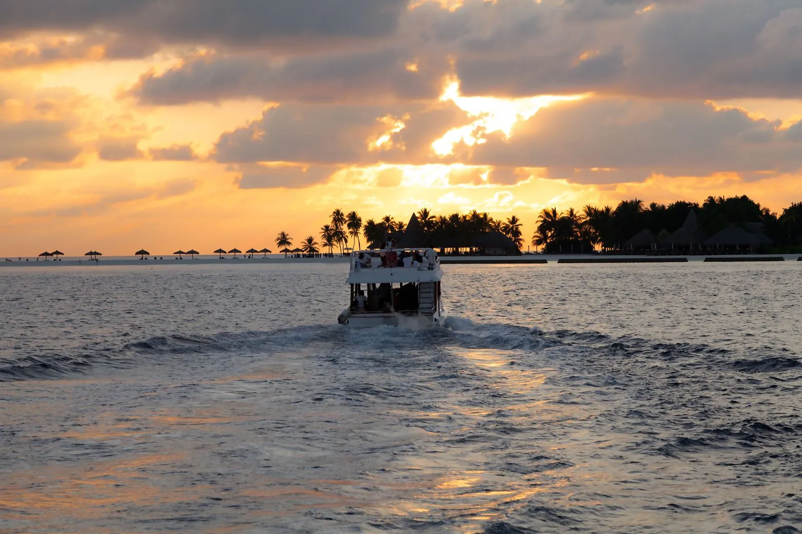 A speedboat on the sea at sunset, heading for an island of palms
