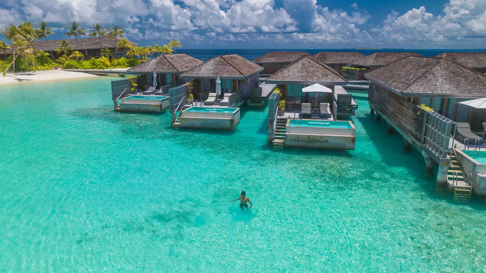 The overwater villas from above, someone swimming in the lagoon in front