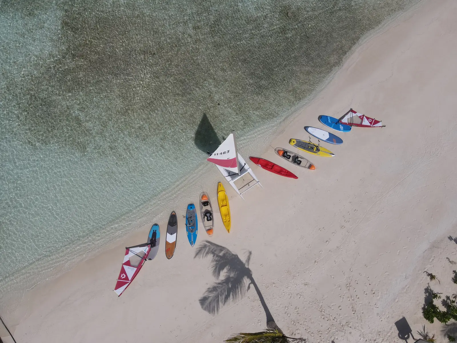 Kayaks and paddleboards lined up on the sand, seen from above