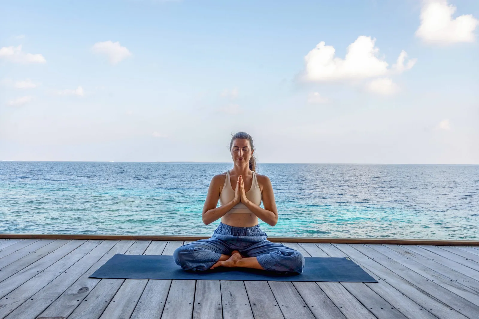 A woman meditating on a deck facing the sea