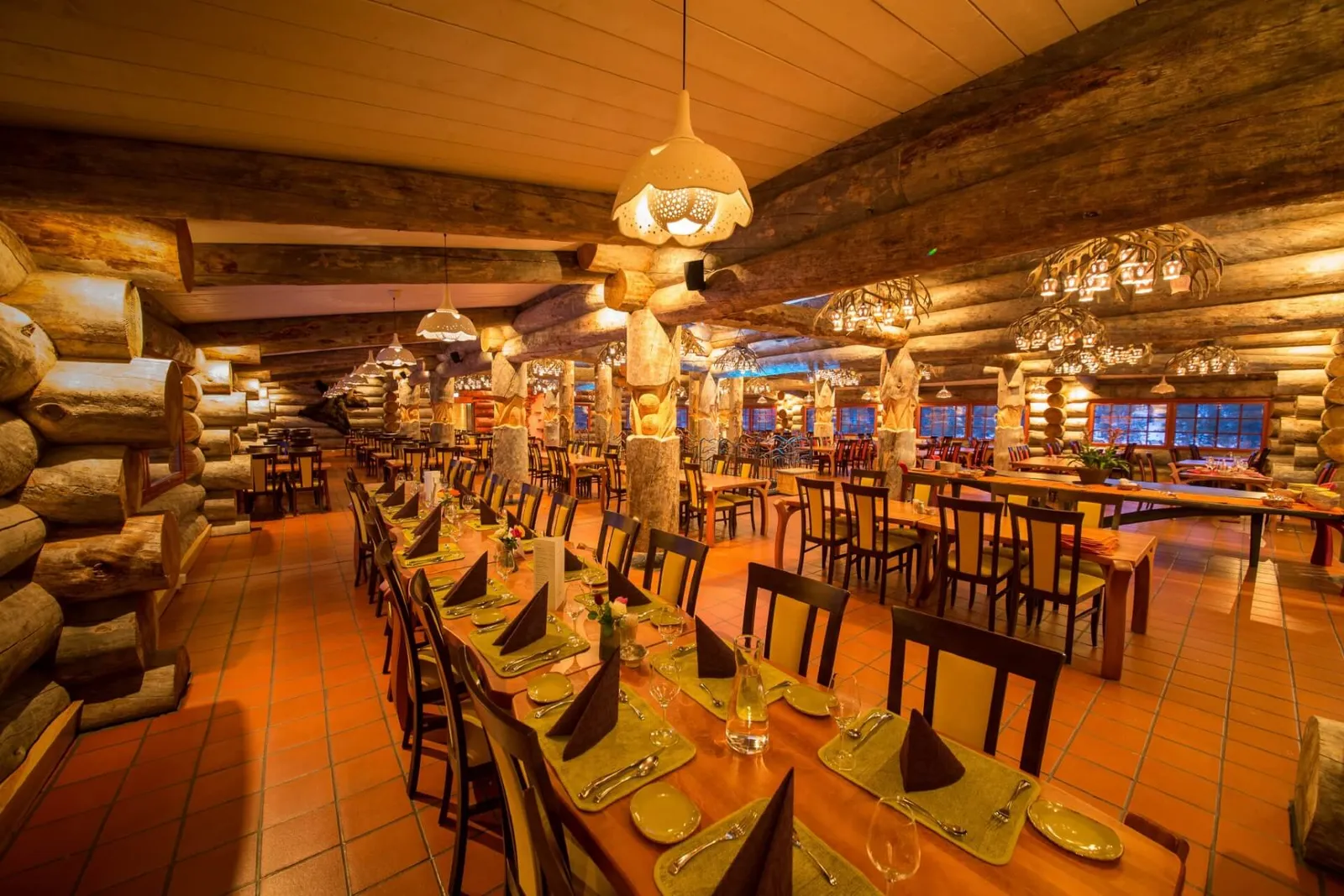 The Aurora Restaurant’s dining room: walls of heavy logs, chandeliers and a long table laid with folded dark napkins.