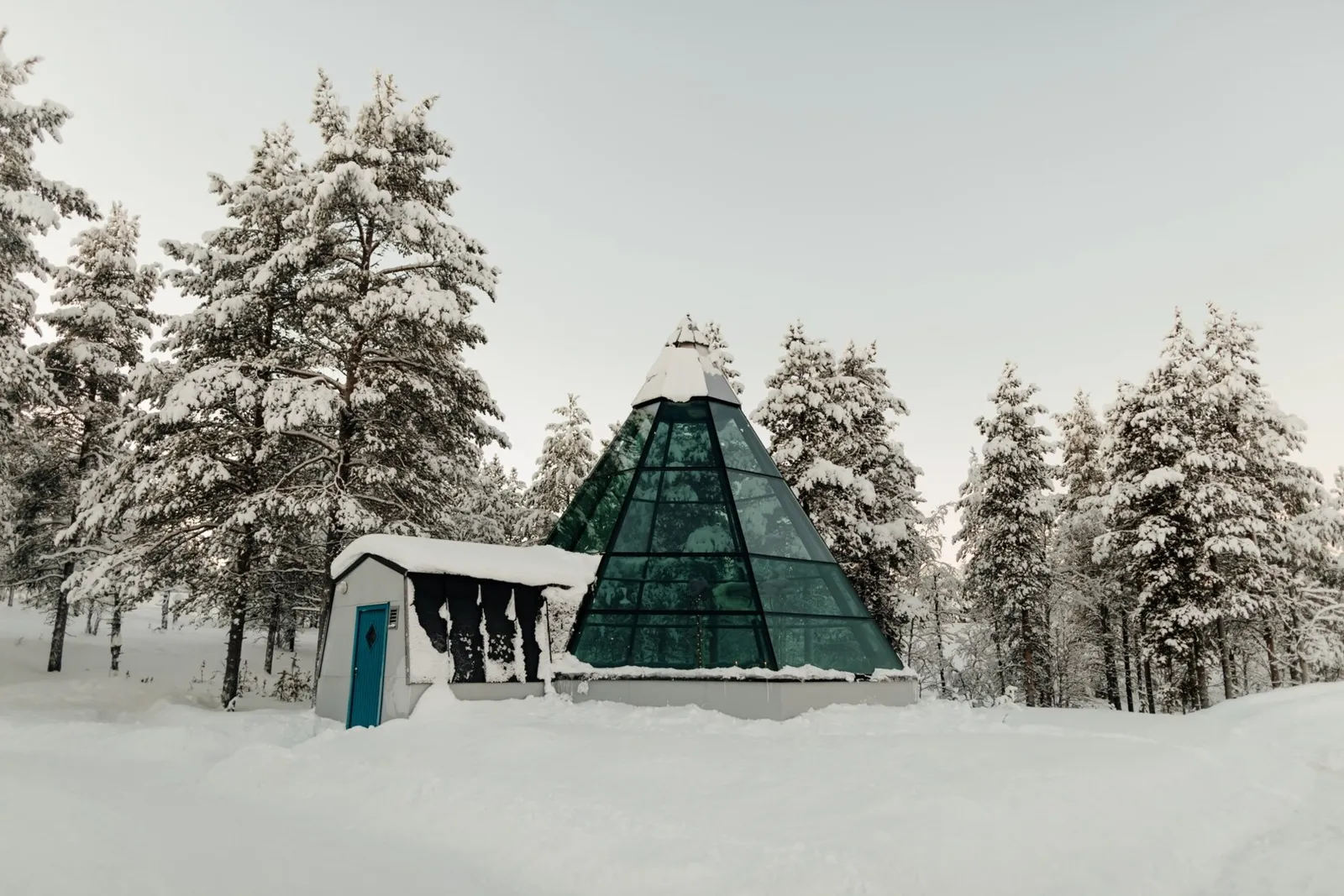 The Glass Teepee, a green glass pyramid with a small white porch, among snowy pines.