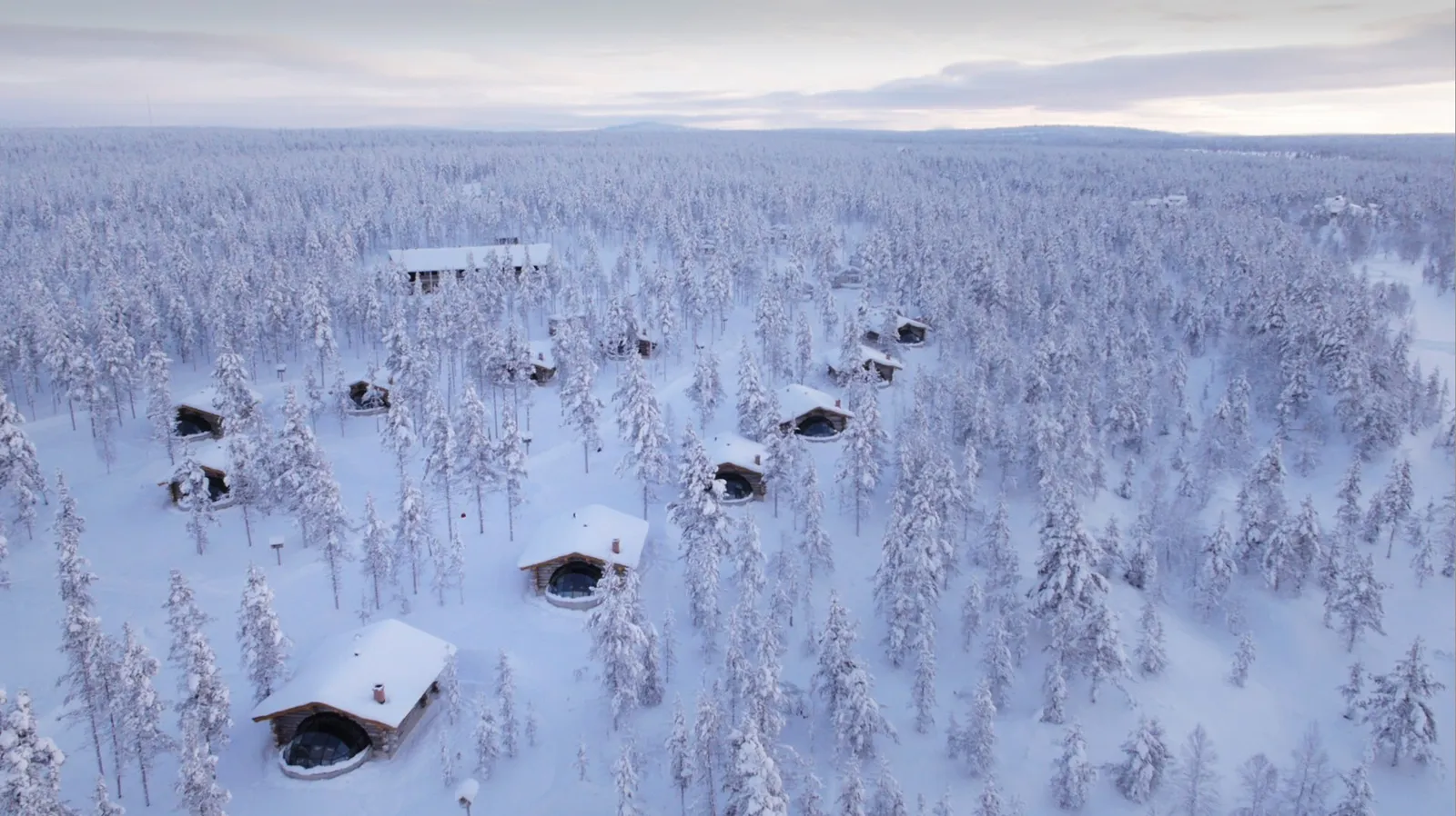 The Kelo-Glass Igloos from the air: log houses with a glass dome scattered through the snowy forest to the horizon.