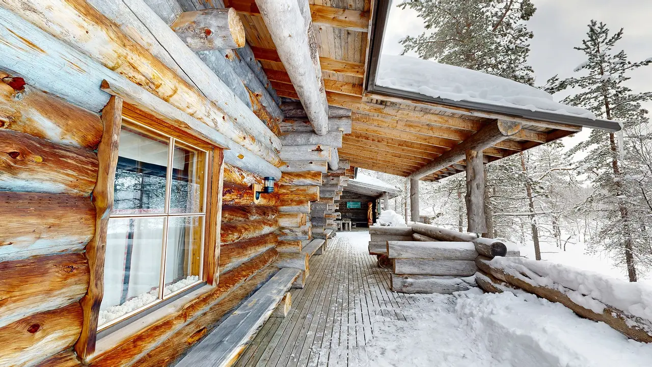 The porch of the large smoke sauna: pale logs, a paned window and the wooden walkway with snow on either side.