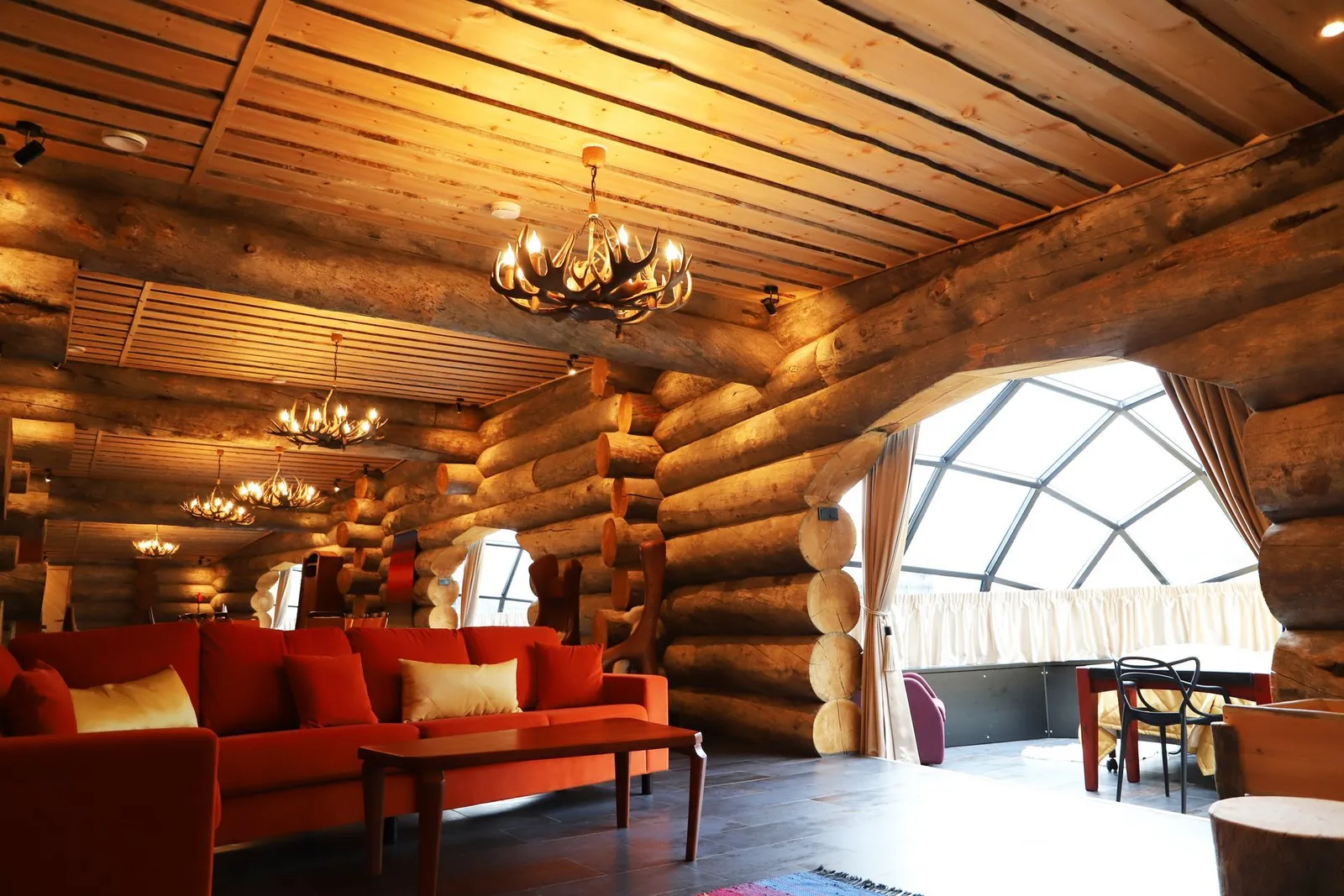 The living room of the Luxury Kelo-Glass Igloo: red sofas, antler chandeliers and an arch opening onto a bedroom with a glass dome.