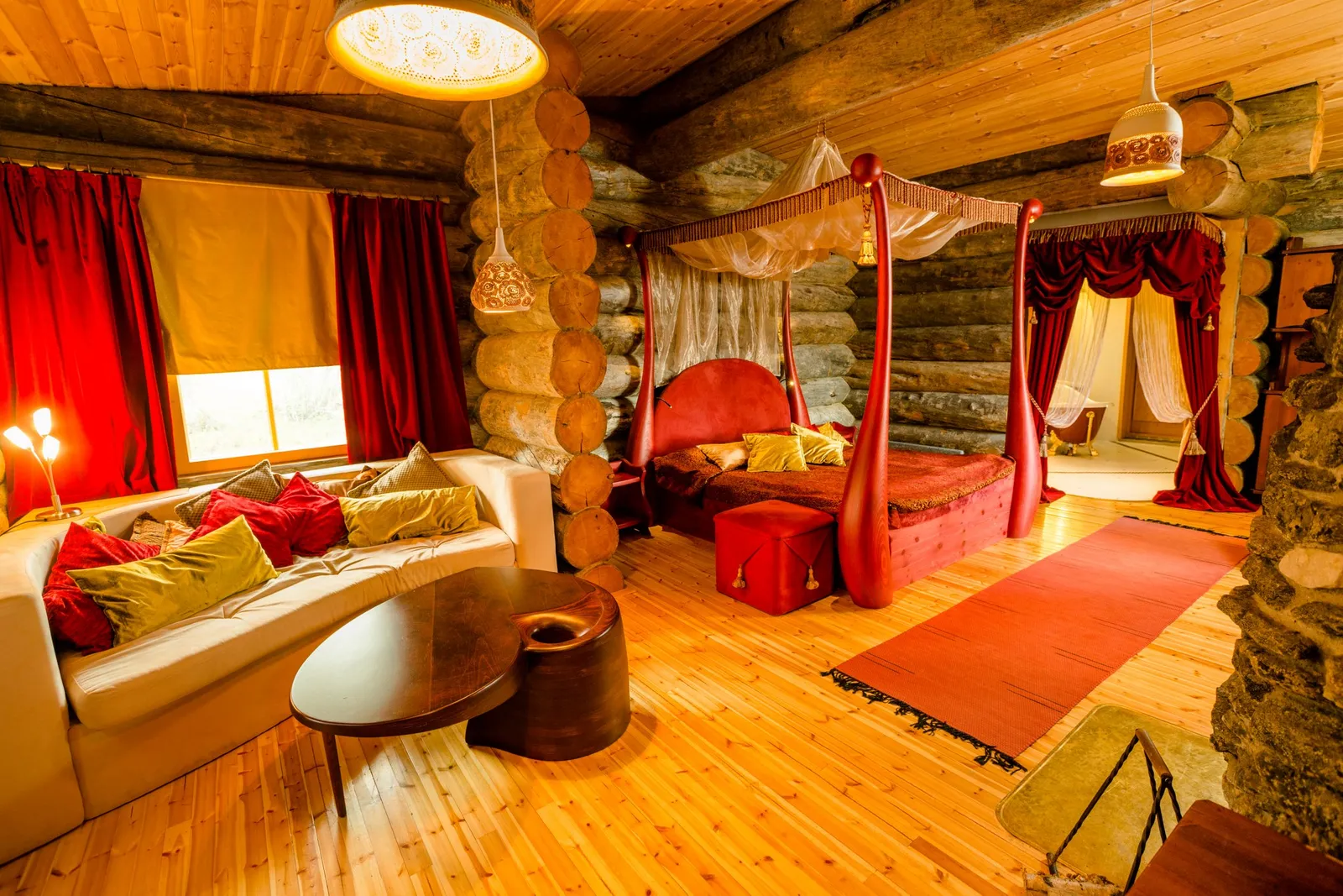 The Queen Suite: the red four-poster bed, the pale sofa with cushions and walls of kelo logs.
