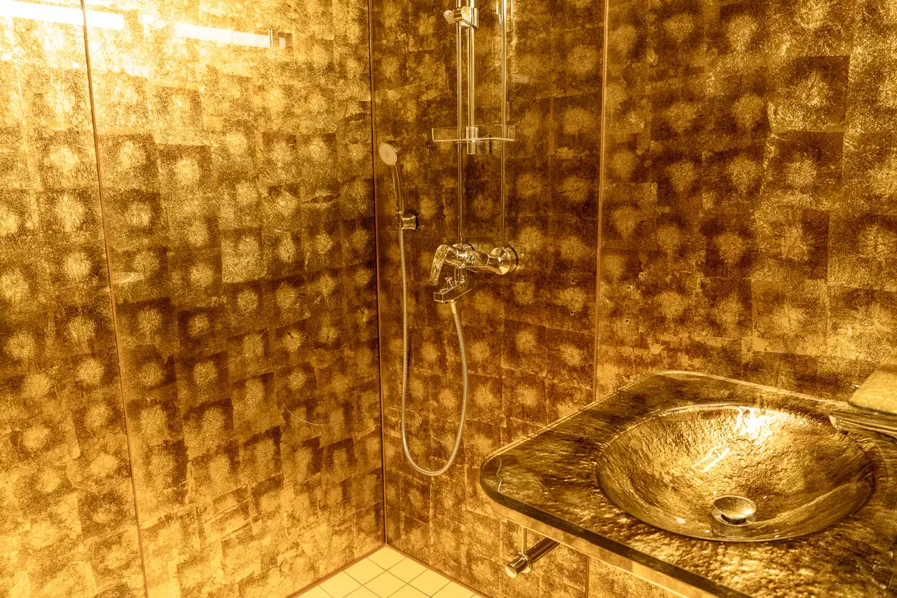 The shower of a Small Glass Igloo: walls faced in gold leaf, the shower head and a gilded glass basin.
