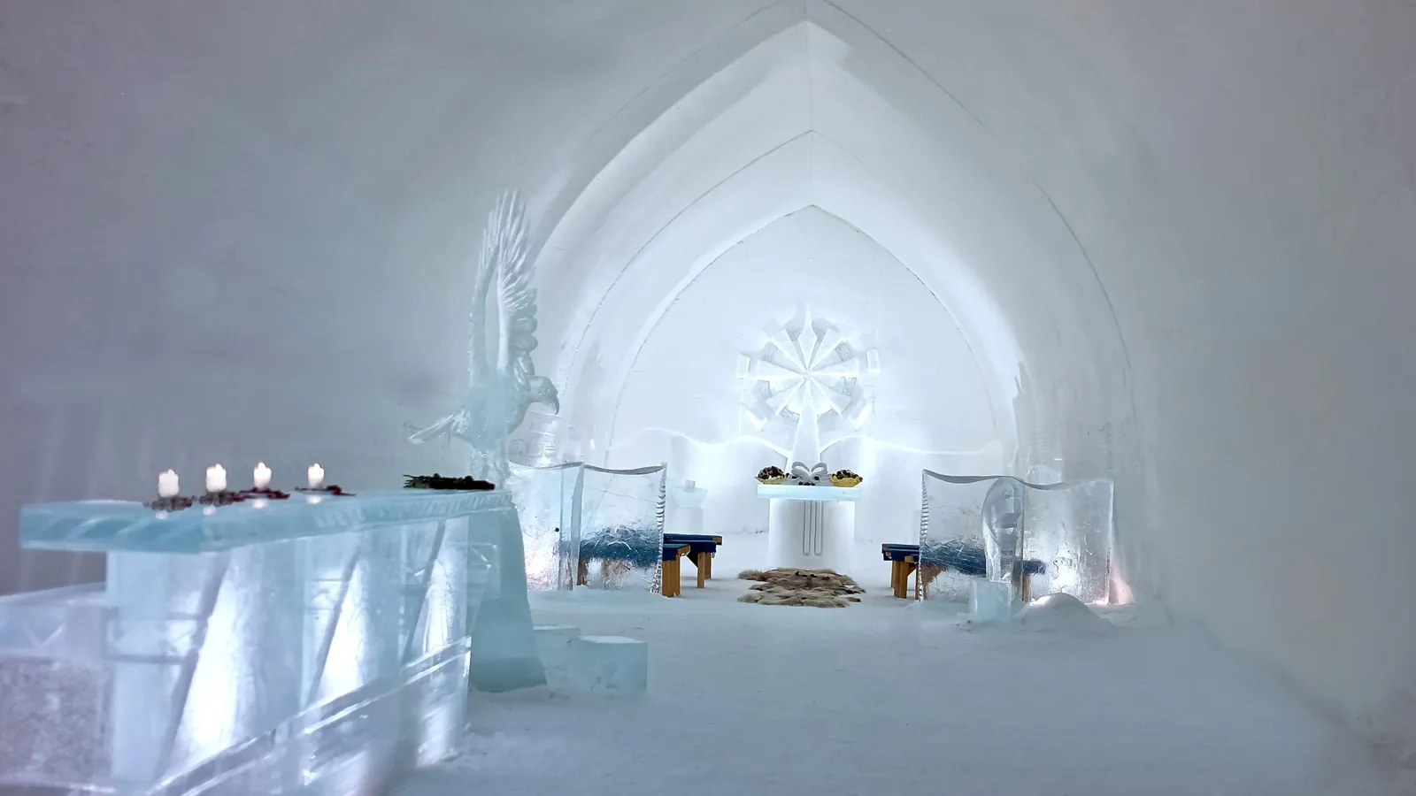 Inside the snow chapel: the pointed vault carved in white, the ice altar with candles and seats of ice.