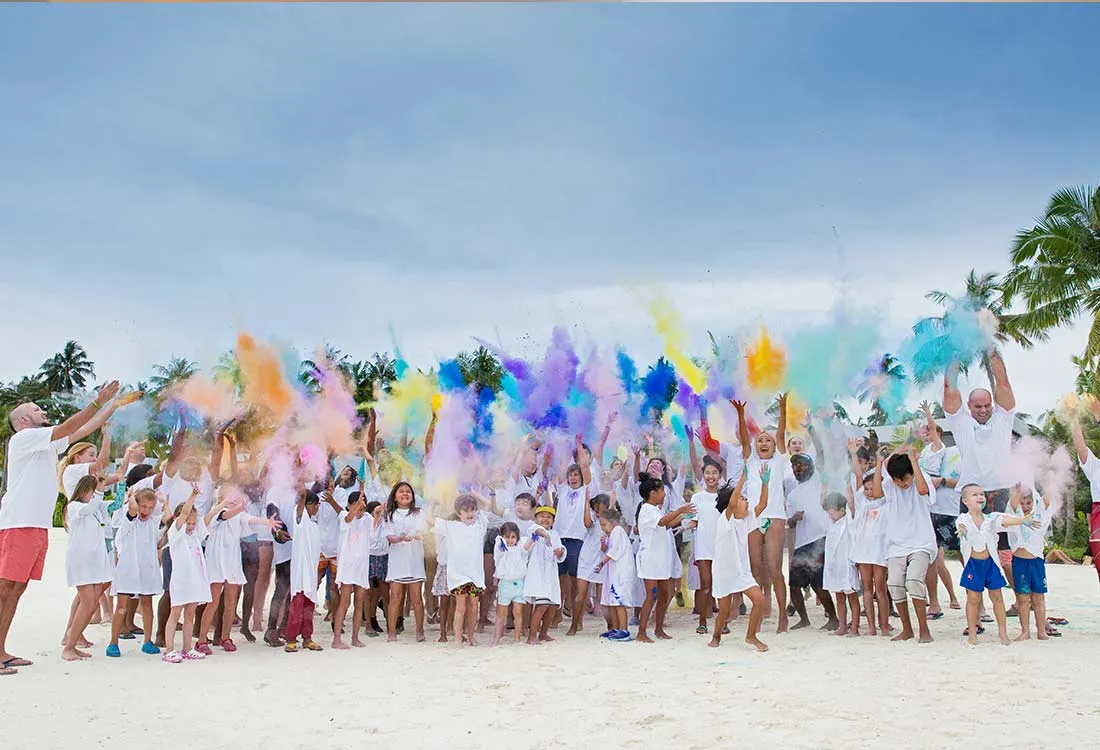 A group dressed in white covered in coloured powder on the beach