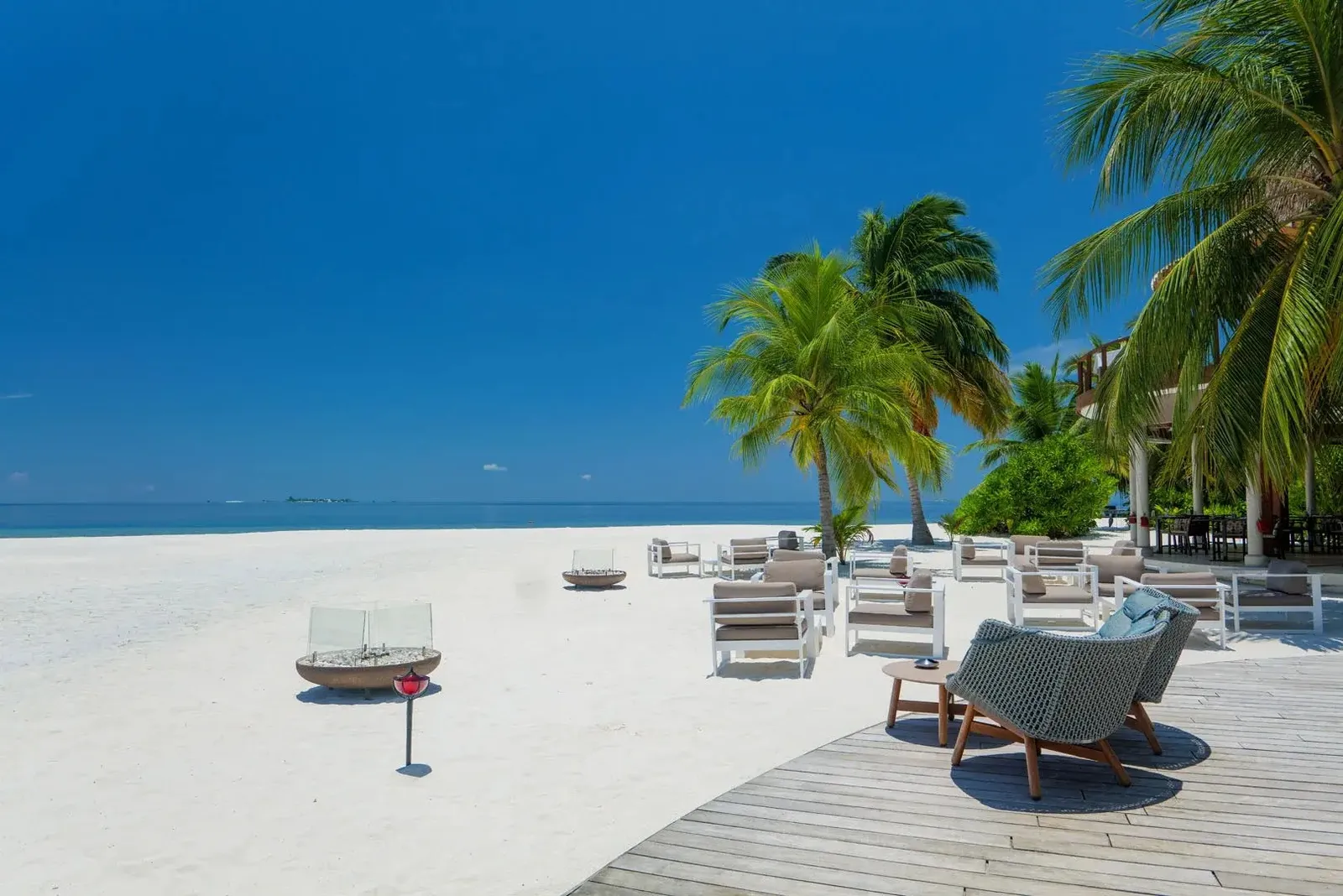 The timber deck on the beach with armchairs and tables, palms around it