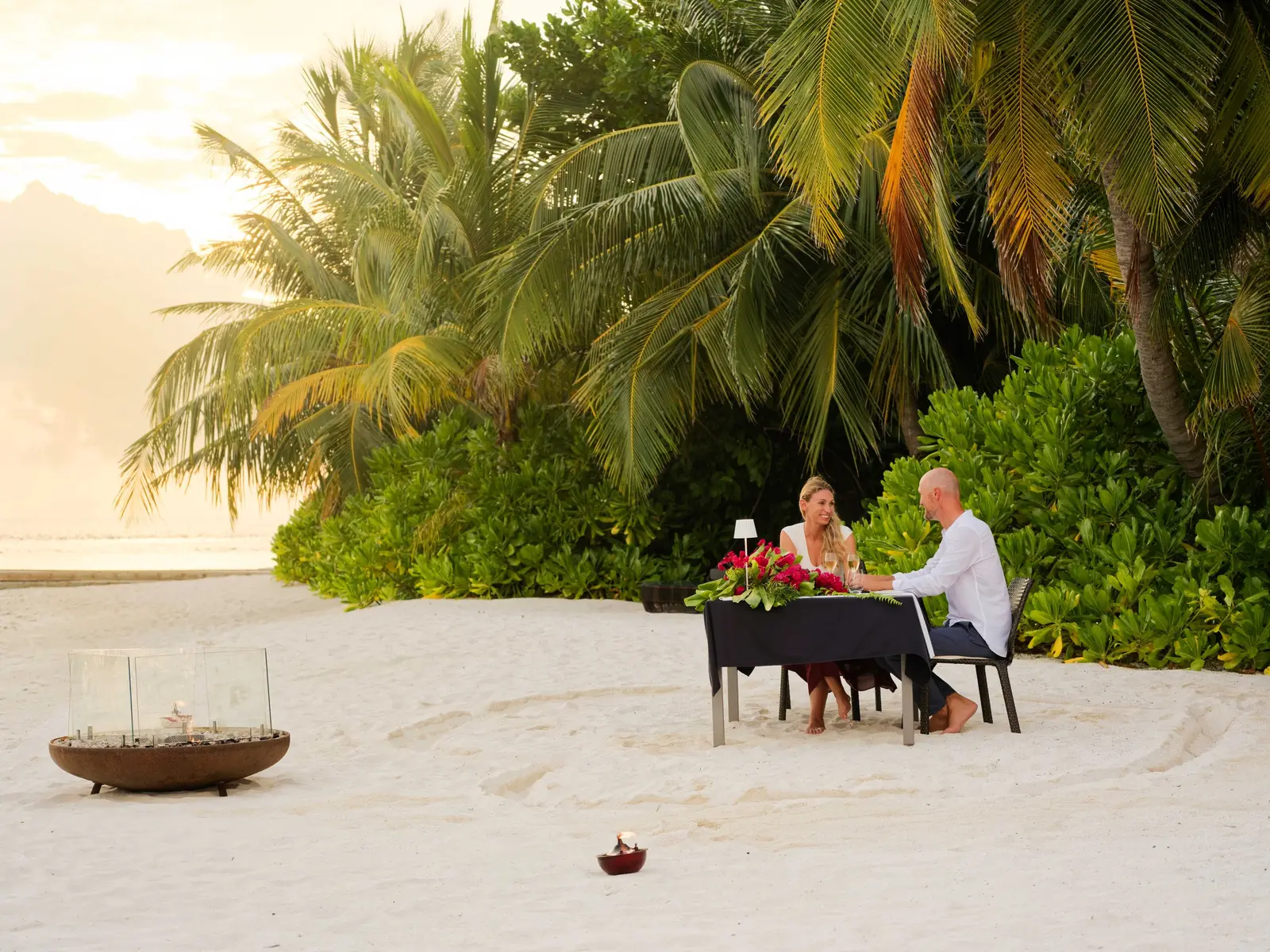 A couple dining on the beach at sunset, a brazier alight