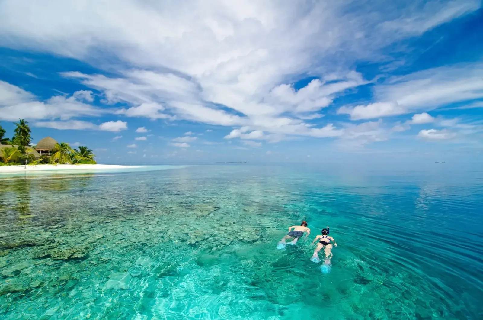 2 people snorkelling in the clear lagoon, the island behind