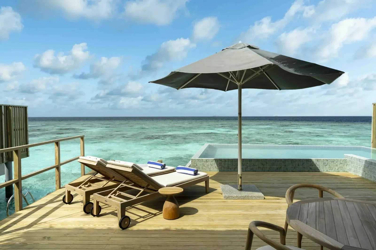 A Deluxe Ocean Pool Villa’s deck with its parasol, loungers and pool over the sea