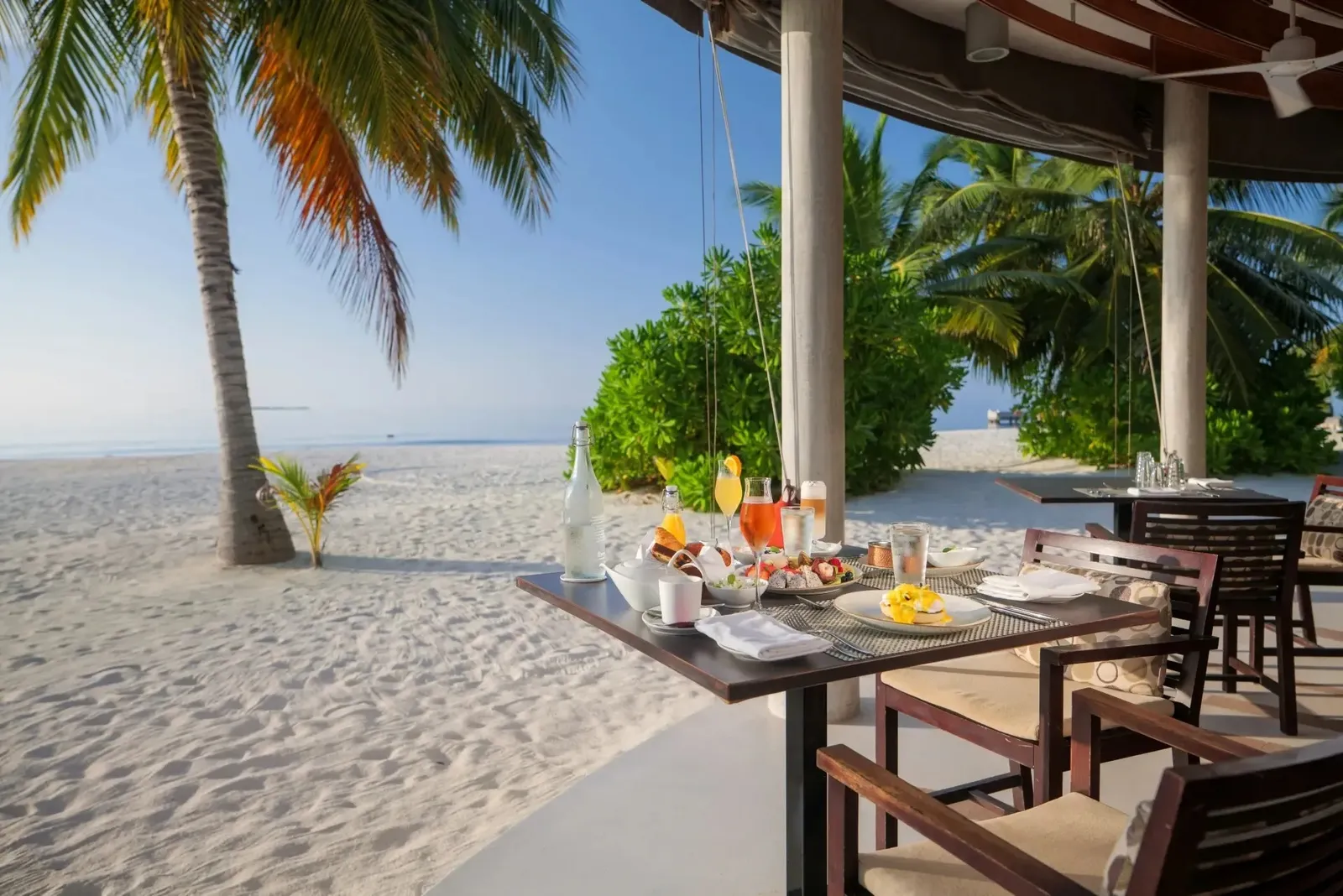 A table laid on the sand outside The Market, the palms and the sea beyond
