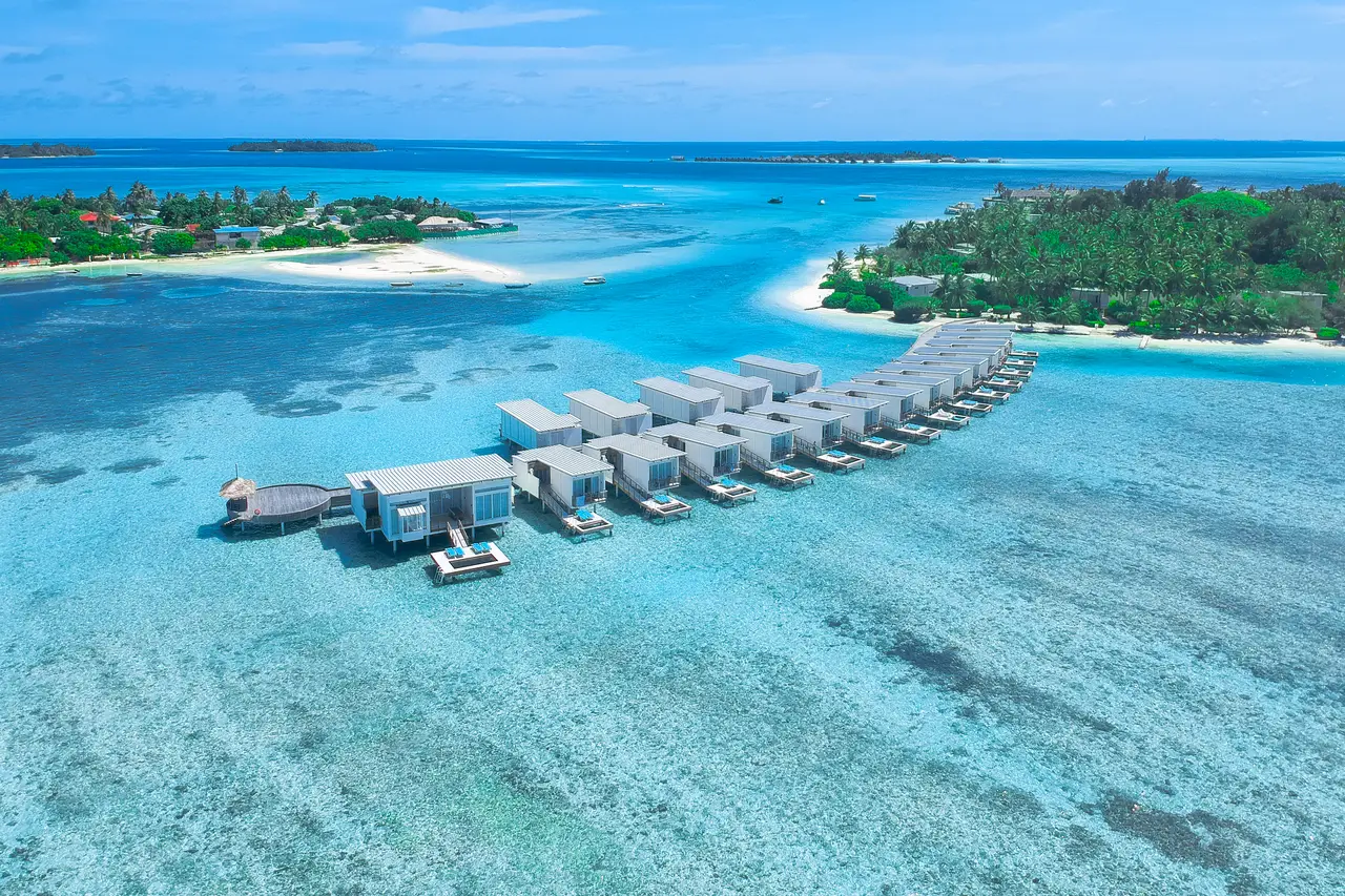 The water villas in a row along their jetty, above the turquoise lagoon, with the green island behind.