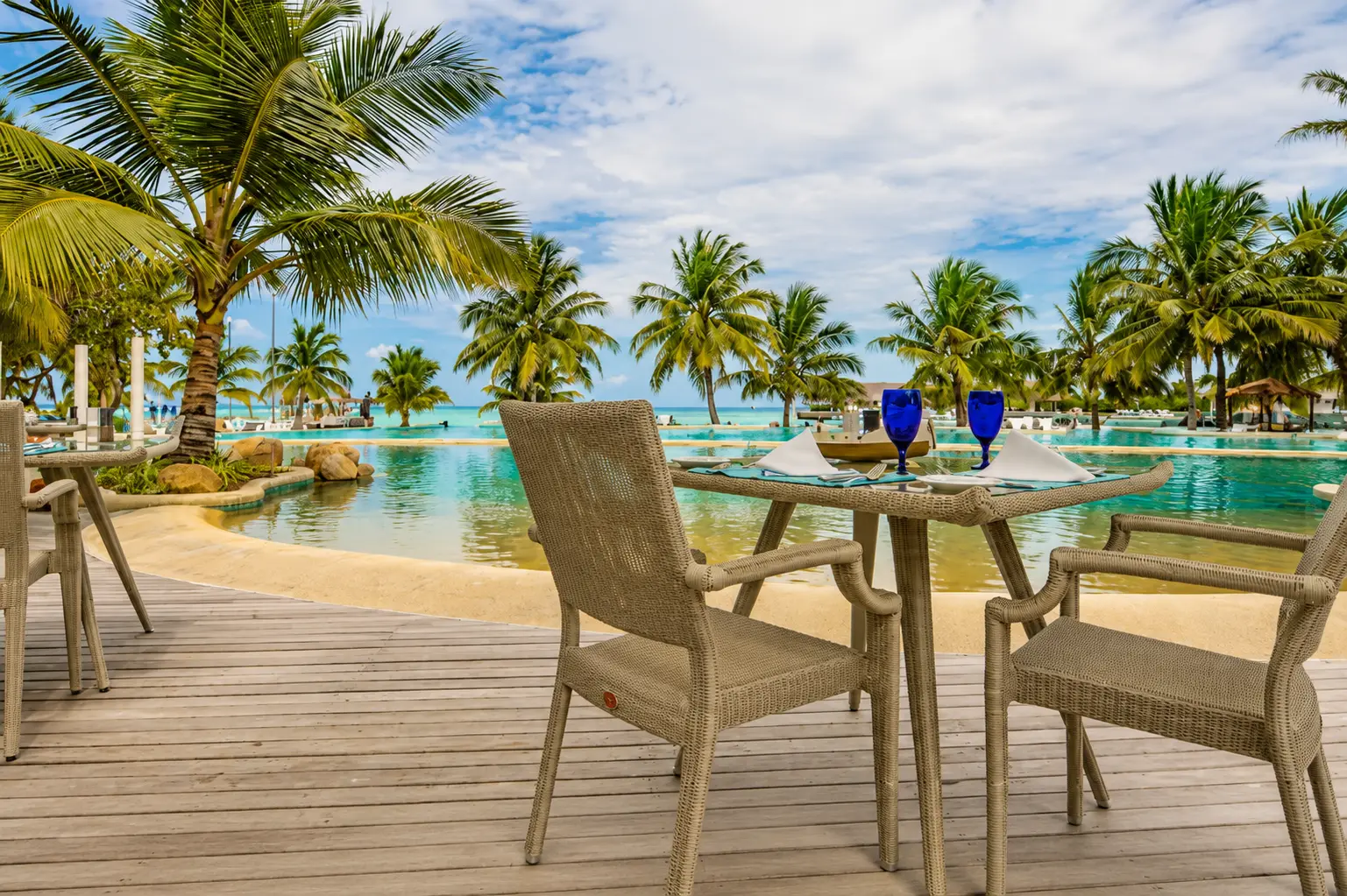 A table laid on the Bokkuraa Pool Deck, with the pool and the palms behind.
