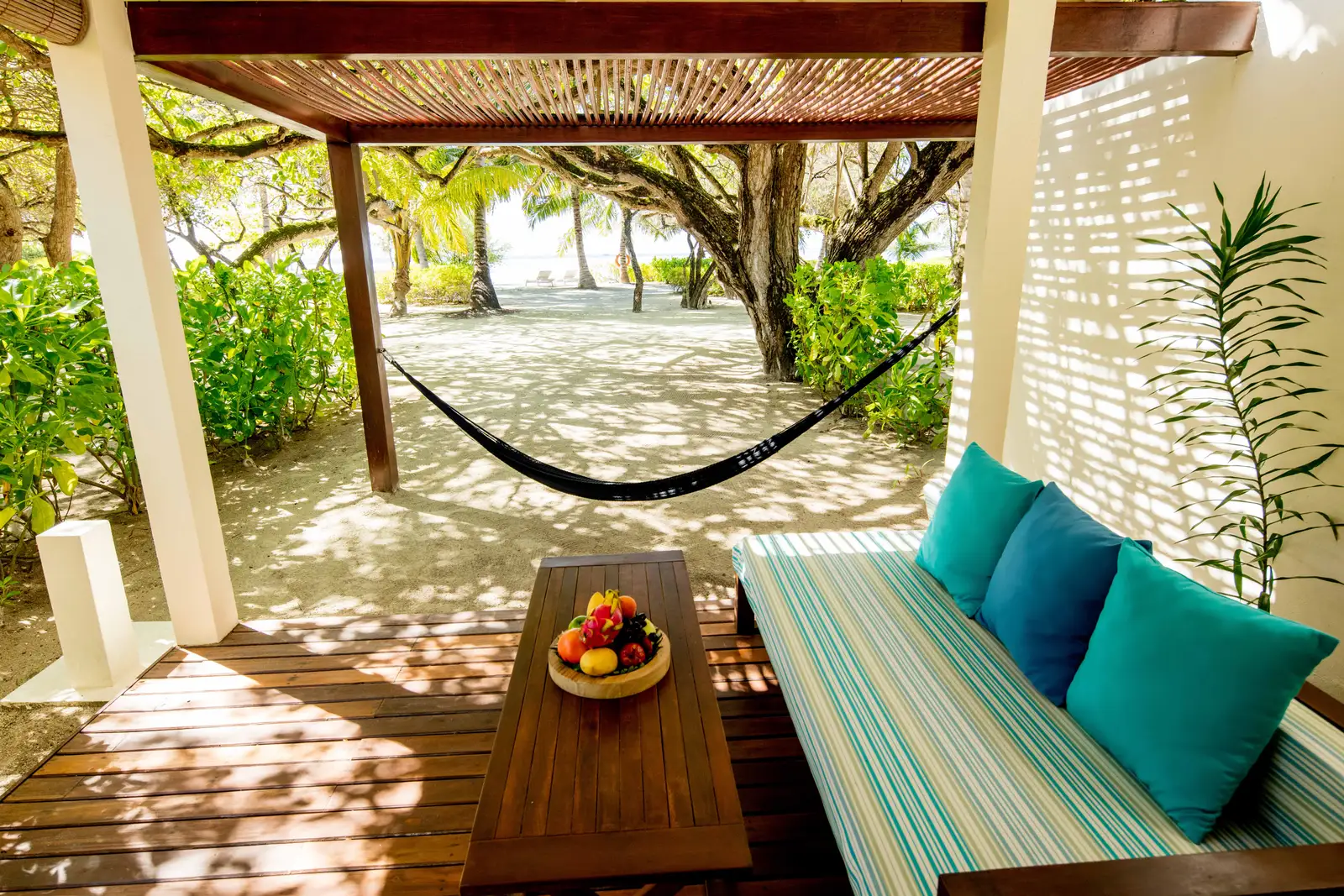 A Beach Villa’s veranda: the striped daybed, the wooden table with fruit and the hammock facing the sand.